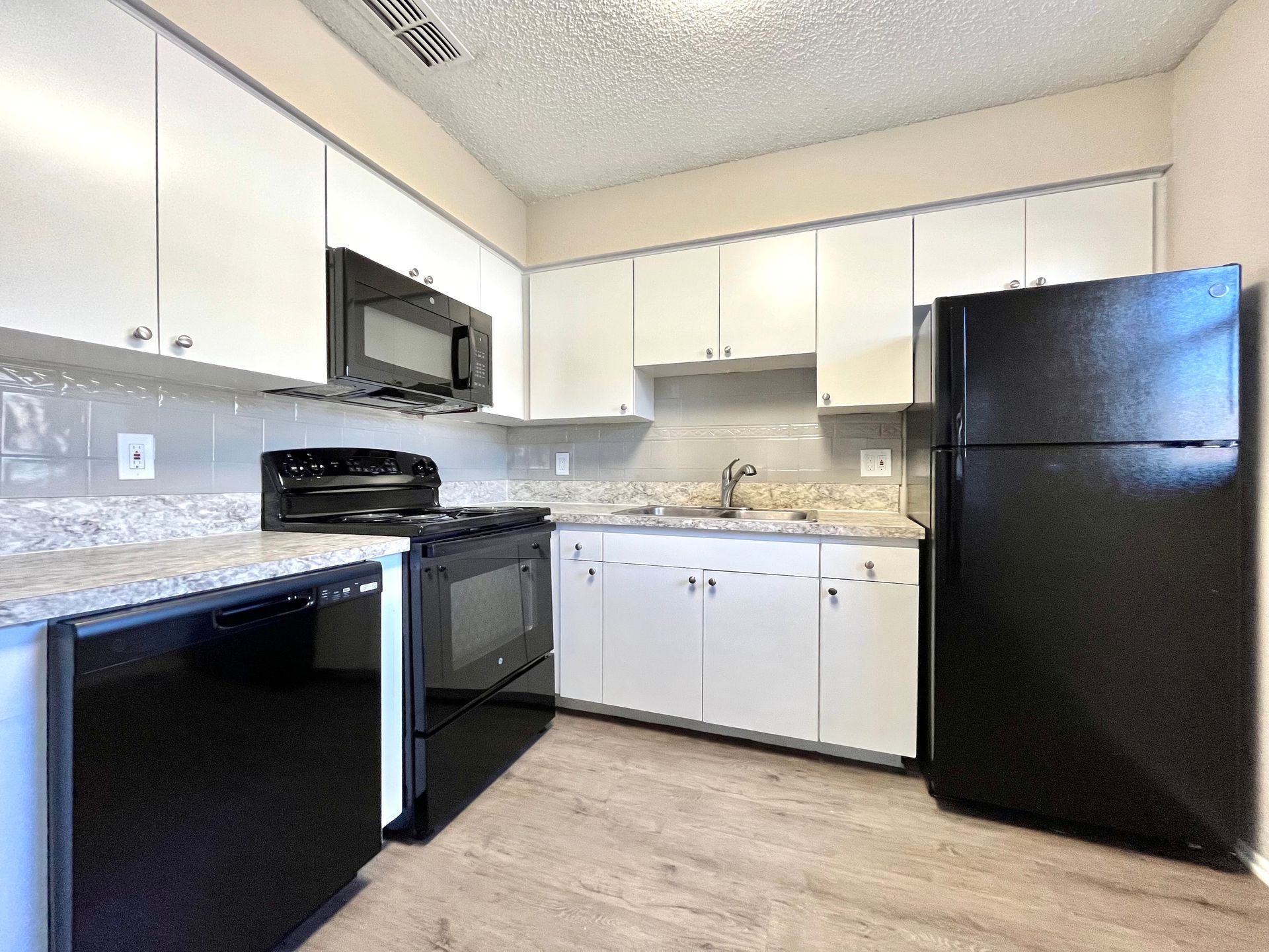 Kitchen with white cabinets, black appliances, and light countertops.