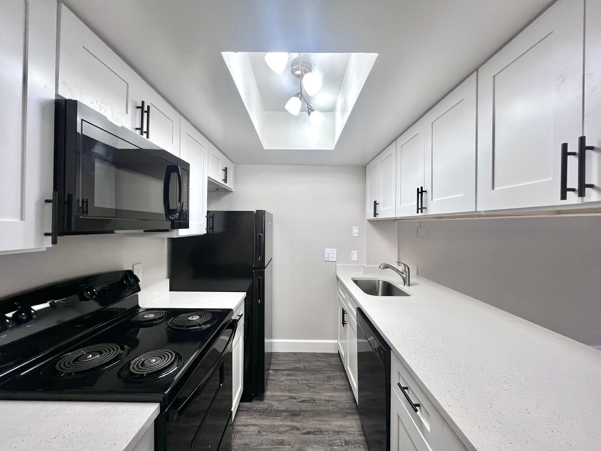 Modern galley kitchen with white cabinets, black appliances, and a skylight.