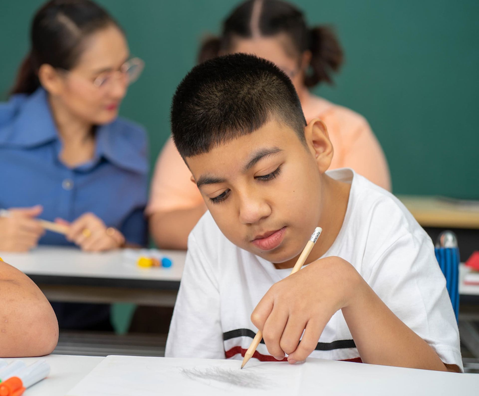 A Boy Is Sitting at A Desk in A Classroom Writing on A Piece of Paper — Psych Solutions NT in Leanyer, NT