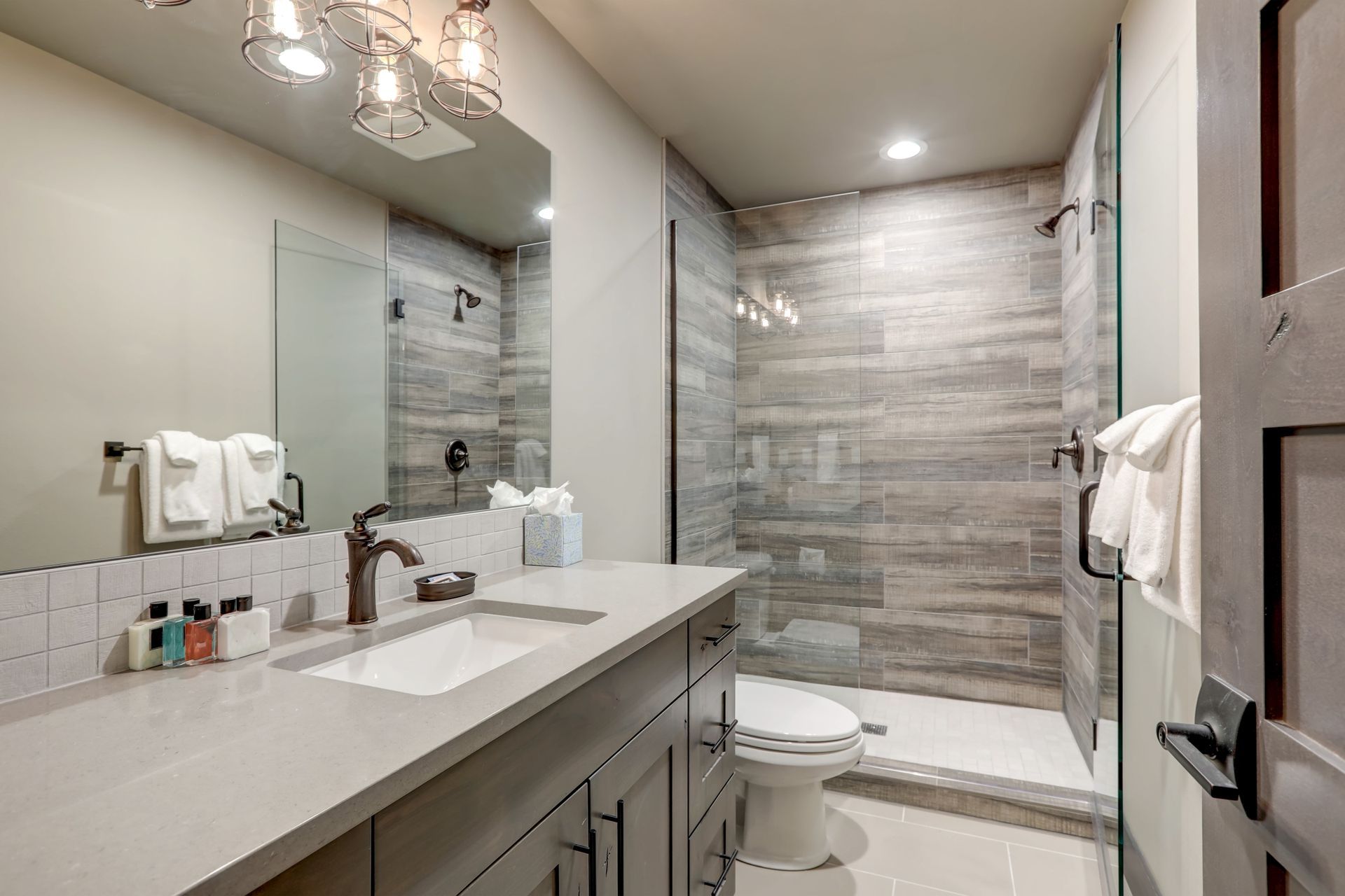 Modern bathroom with double vanity, large mirror, glass shower, and toilet in gray tones