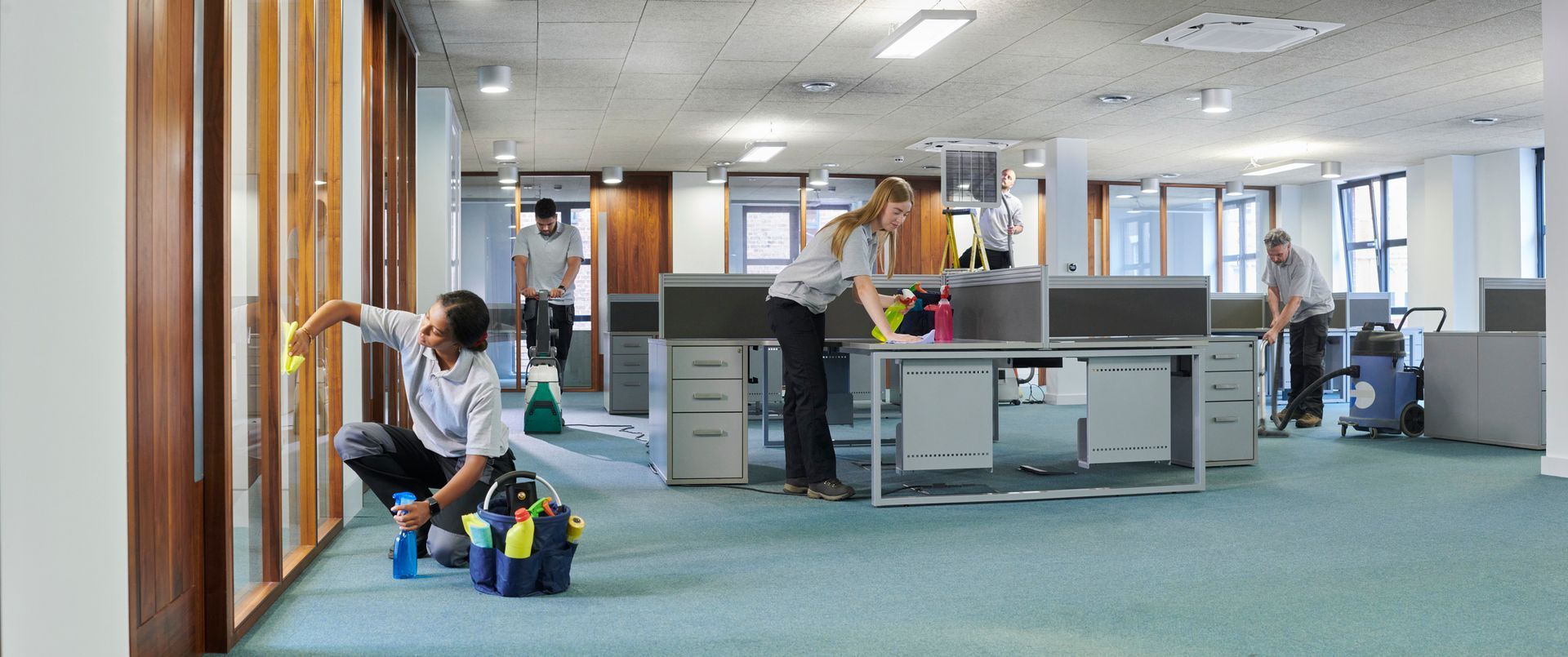 Una persona con tuta protettiva spruzza acqua sul marciapiede fuori da un negozio, presumibilmente per igienizzare.