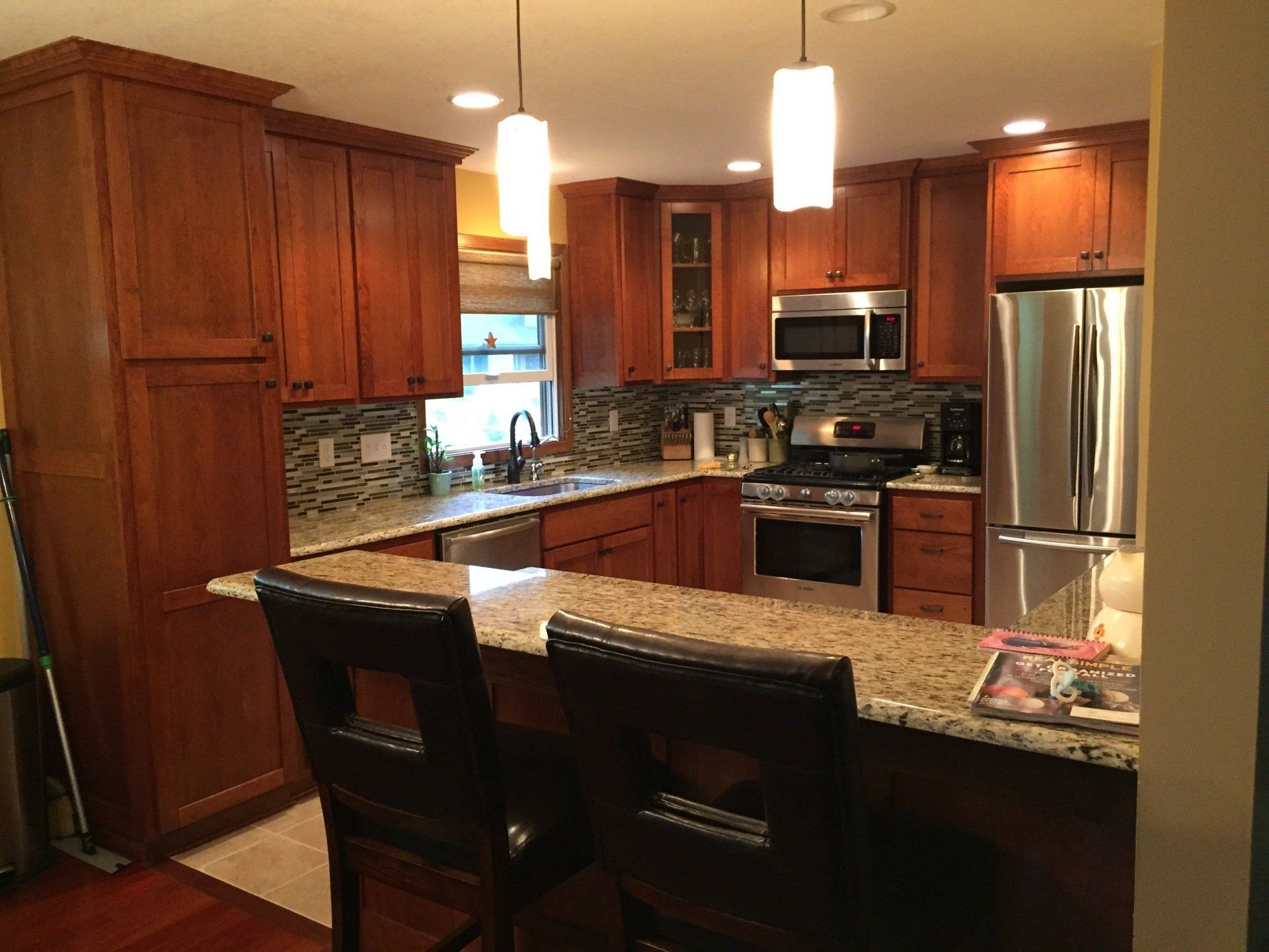 Cozy kitchen with wooden cabinets, granite countertops, stainless steel appliances, and a breakfast bar with two chairs.