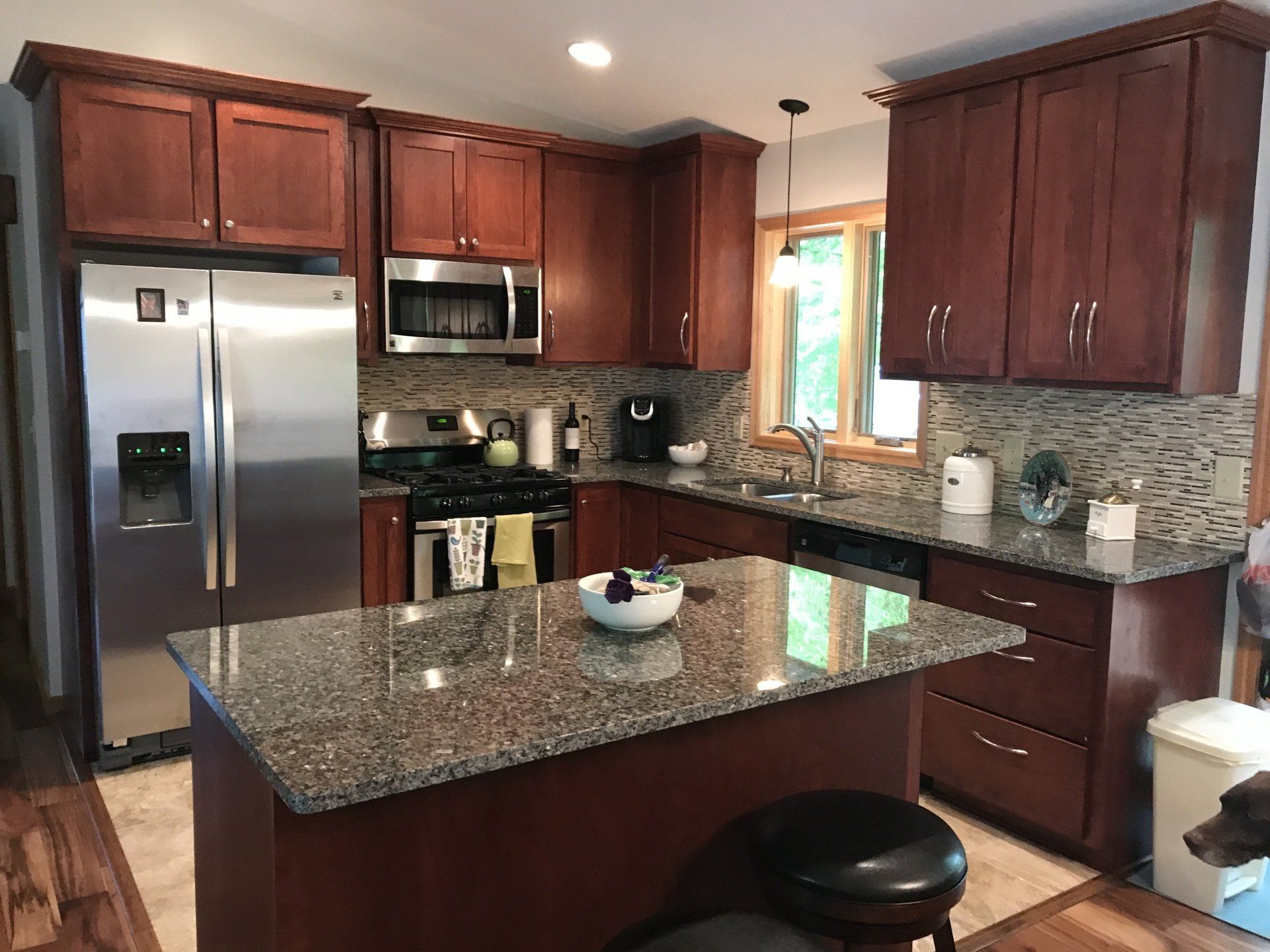 A kitchen with cherry wood cabinets, stainless steel appliances, granite countertops, and an island.