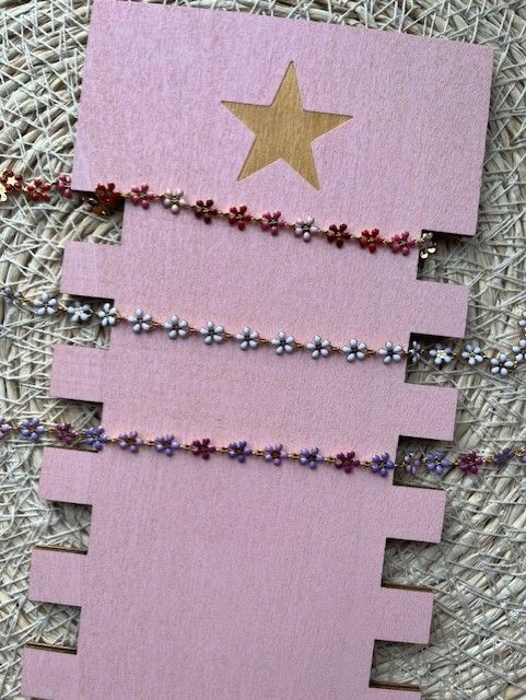 Drie delicate, bloemvormige bedelarmbandjes in rode, blauwe en paarse tinten, gepresenteerd op een roze, gegroefde displaykaart.