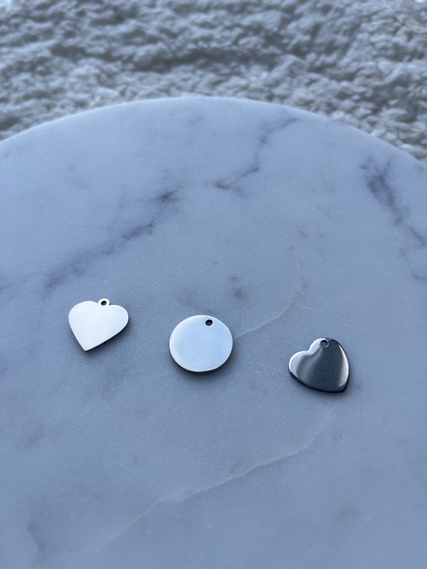 Verschillende gepersonaliseerde kettingen met hart- en ronde hangers liggen uitgestald op een marmeren ondergrond naast een klein mauve fluwelen zakje.