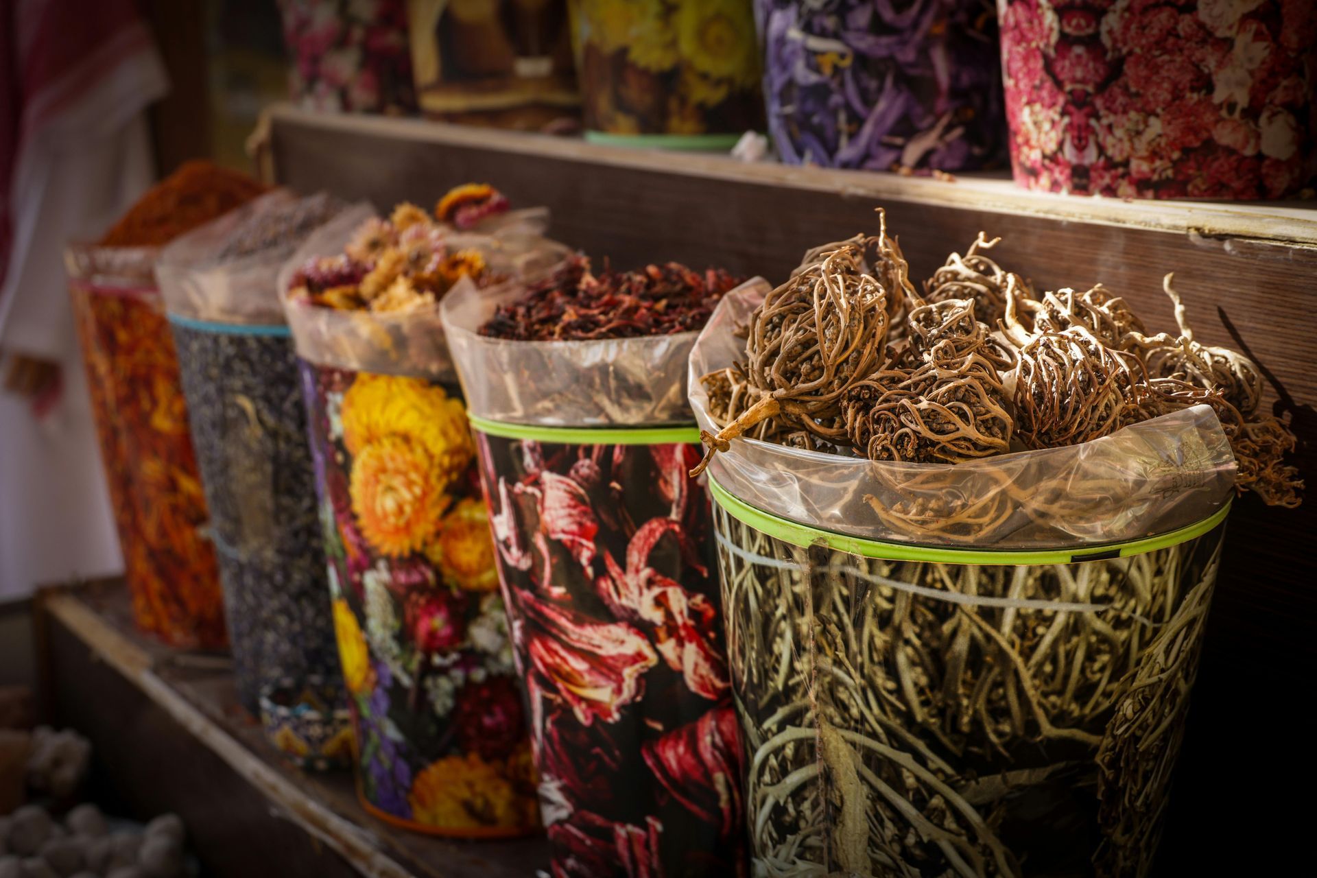 Colorful spice containers on a wooden shelf, various dried herbs and flowers, market.