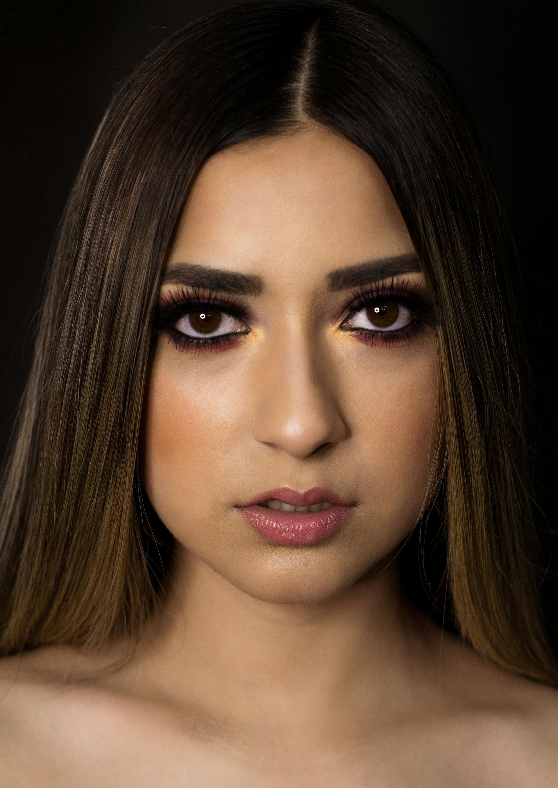 Woman with brown, crimped hair and dramatic eye makeup, looking directly at the camera.