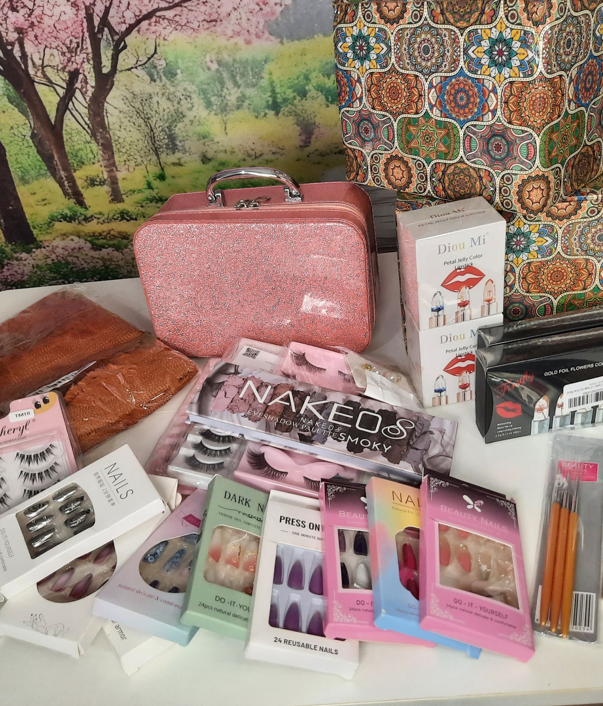 Pink glitter makeup case and various beauty products, including false nails and lashes, on a white surface.