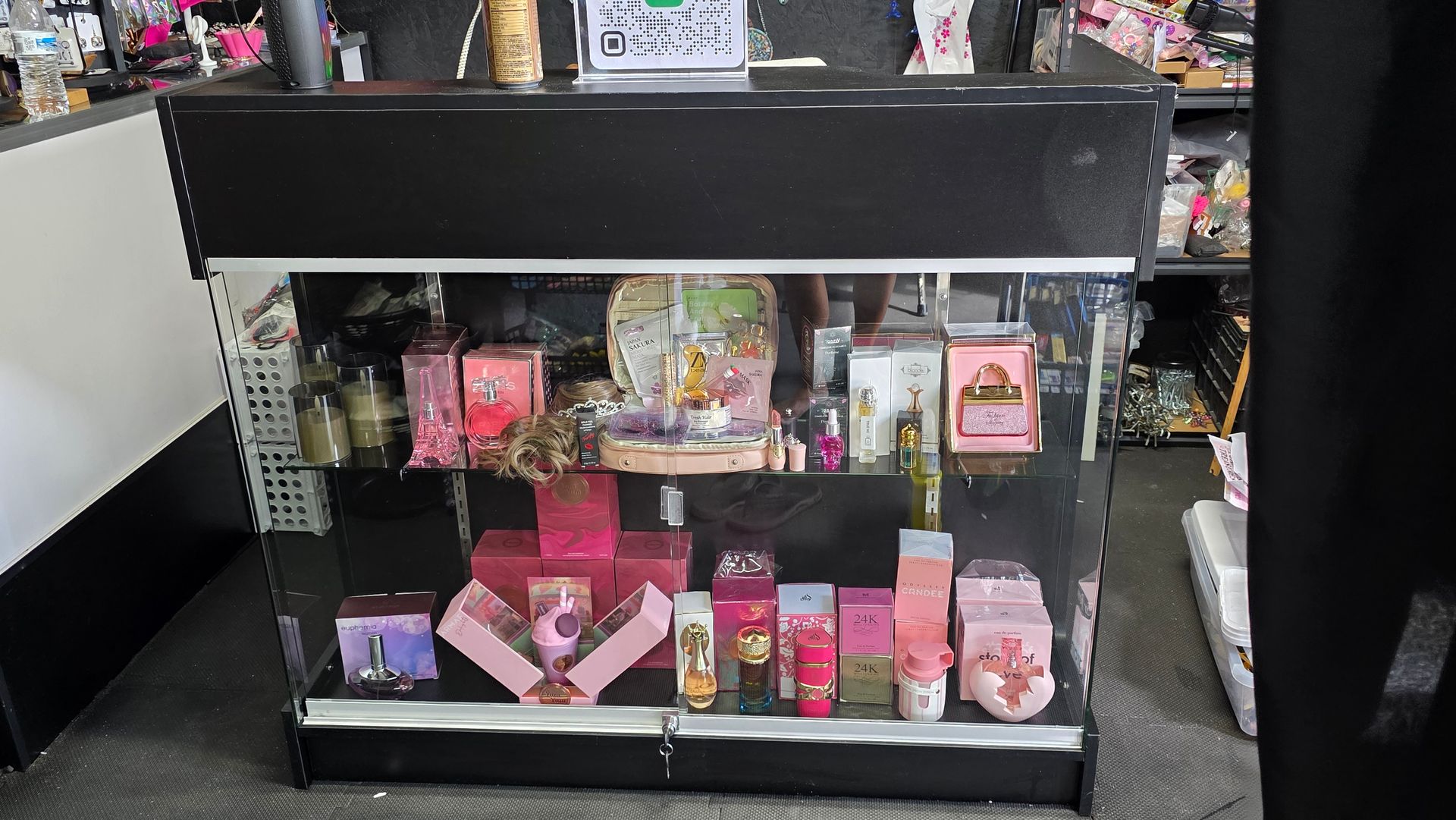 Black display case filled with pink and gold perfumes and beauty products in a store.