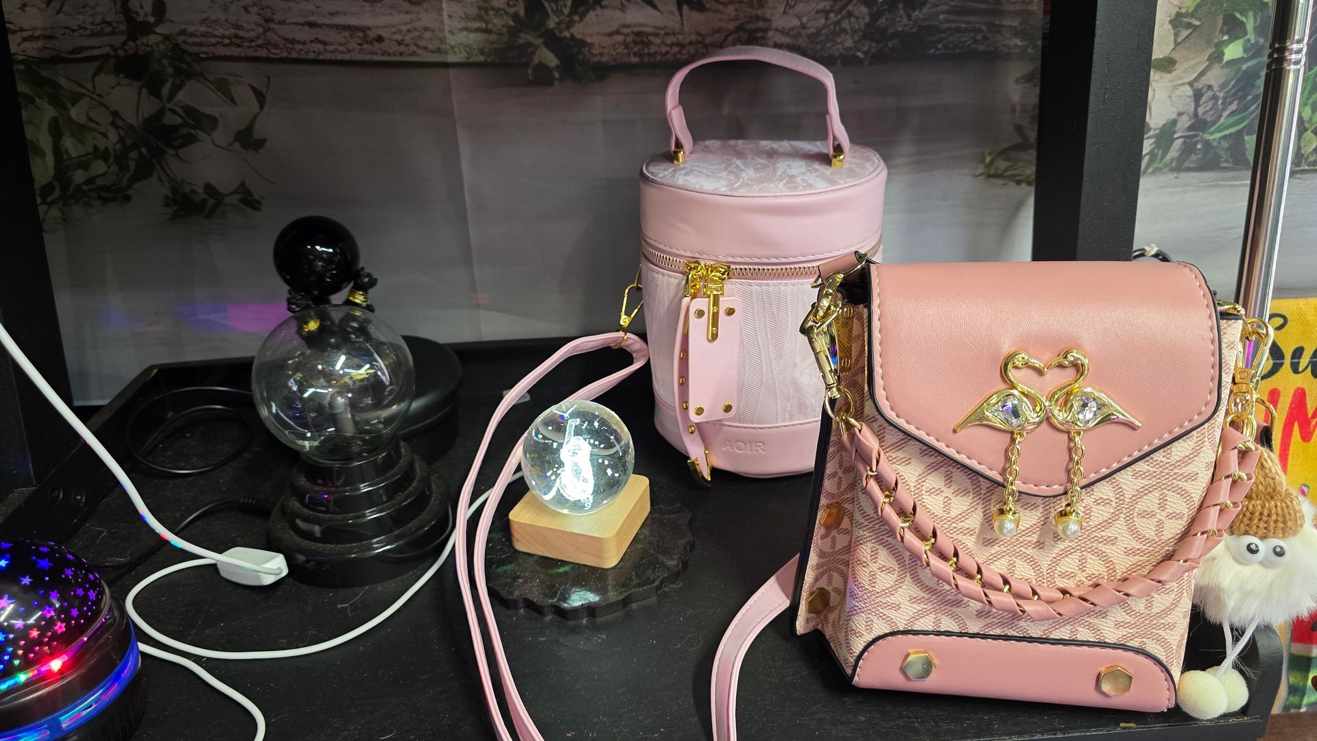 Pink handbags with accessories on a black table: a lamp, snow globe, and a star projector.