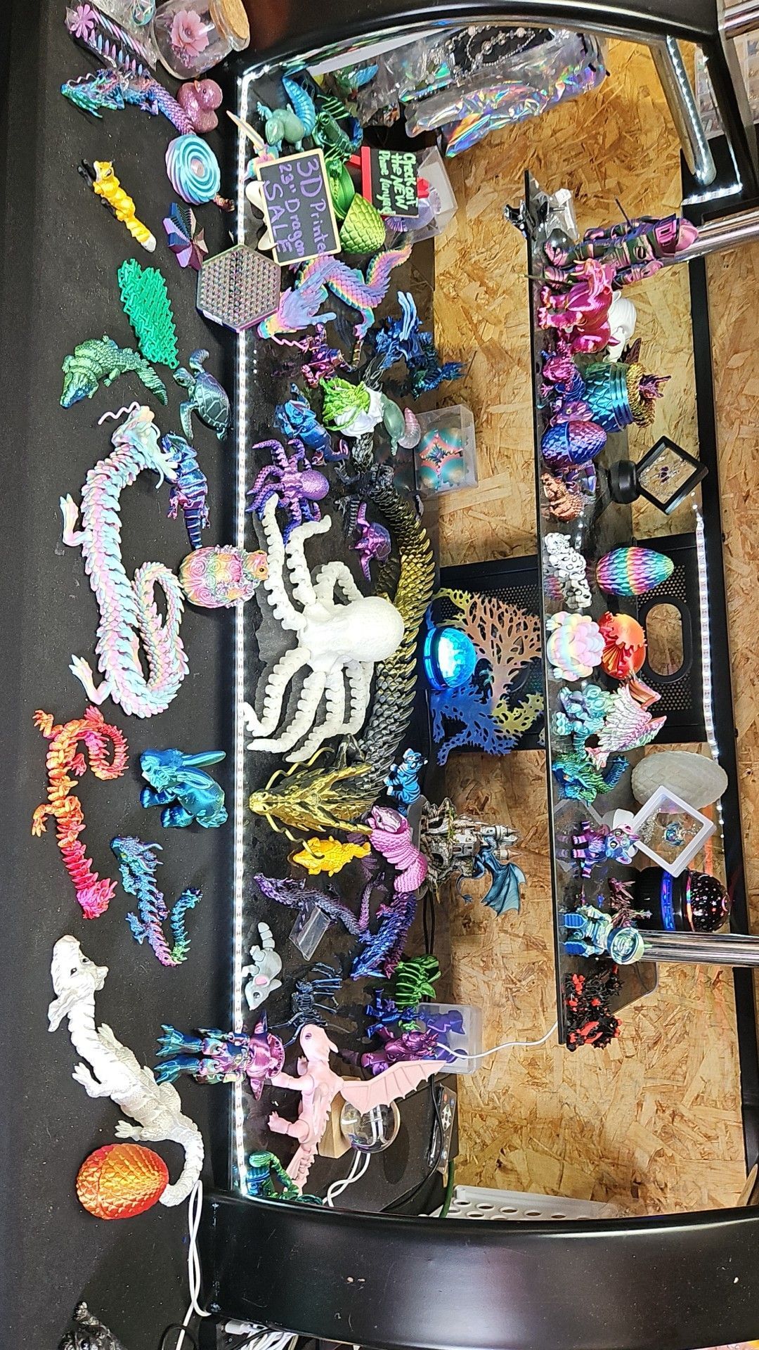 Collection of colorful bead-art creatures, including dragons and octopuses, displayed in a lit, black case.