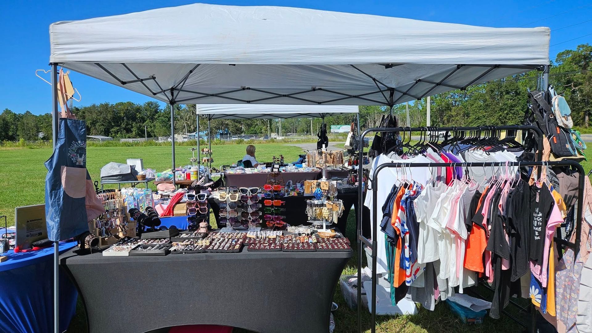 Outdoor market stall with clothes rack, jewelry displays, and canopy tent.