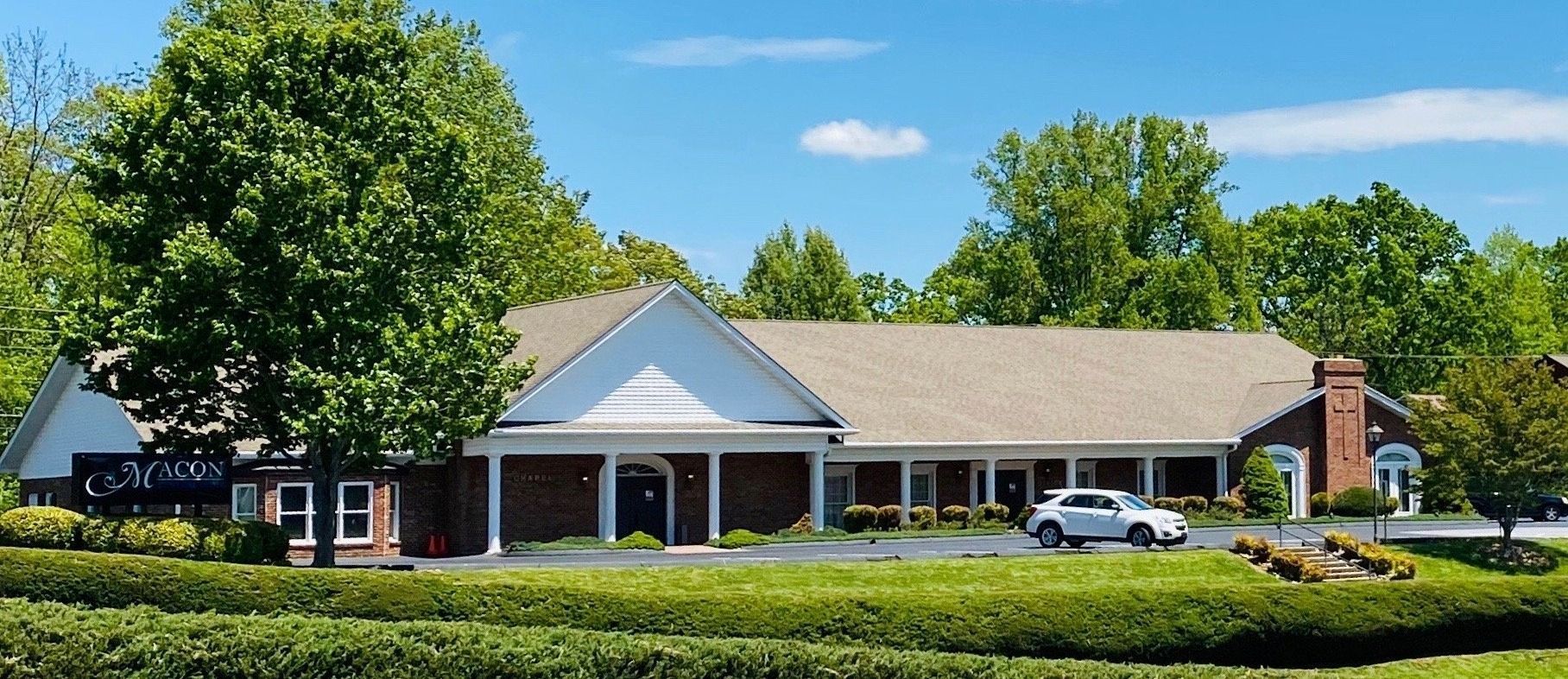 Building with a brick facade and a white entryway, with a tree and green bushes in front.