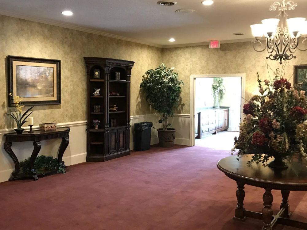 An interior room with a red carpet, dark wood furniture, and floral arrangements.