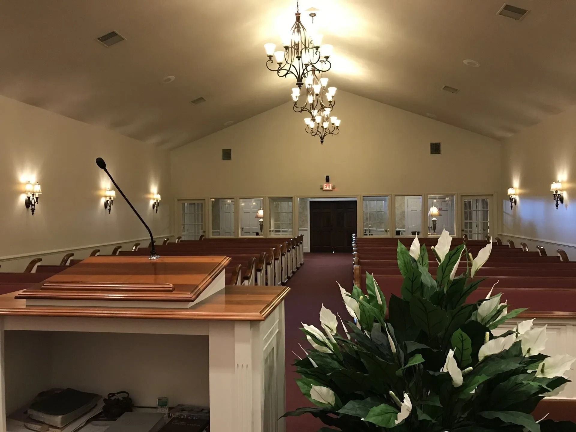 Interior of a chapel with rows of pews, a podium, and a chandelier; flowers in the foreground.