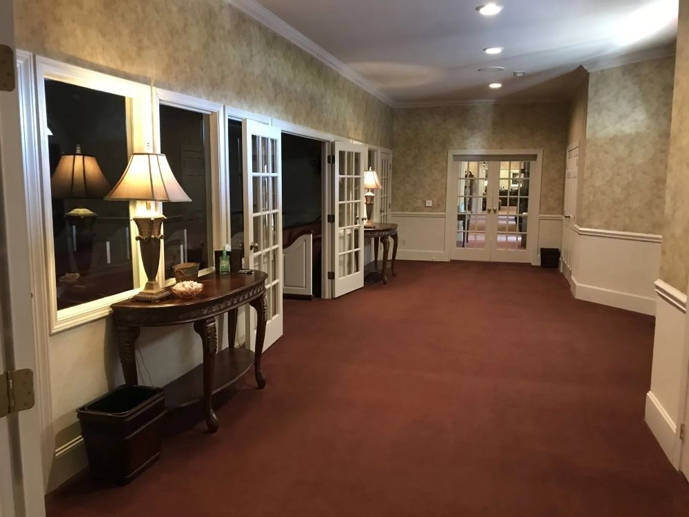 Hallway with red carpet, wallpaper, French doors, table with lamp.