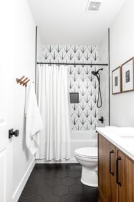 Small white bathroom with black hex tile, white shower curtain, patterned wallpaper, and wood vanity. Small white bathroom with black hex tile, white shower curtain, patterned wallpaper, and wood vanity.