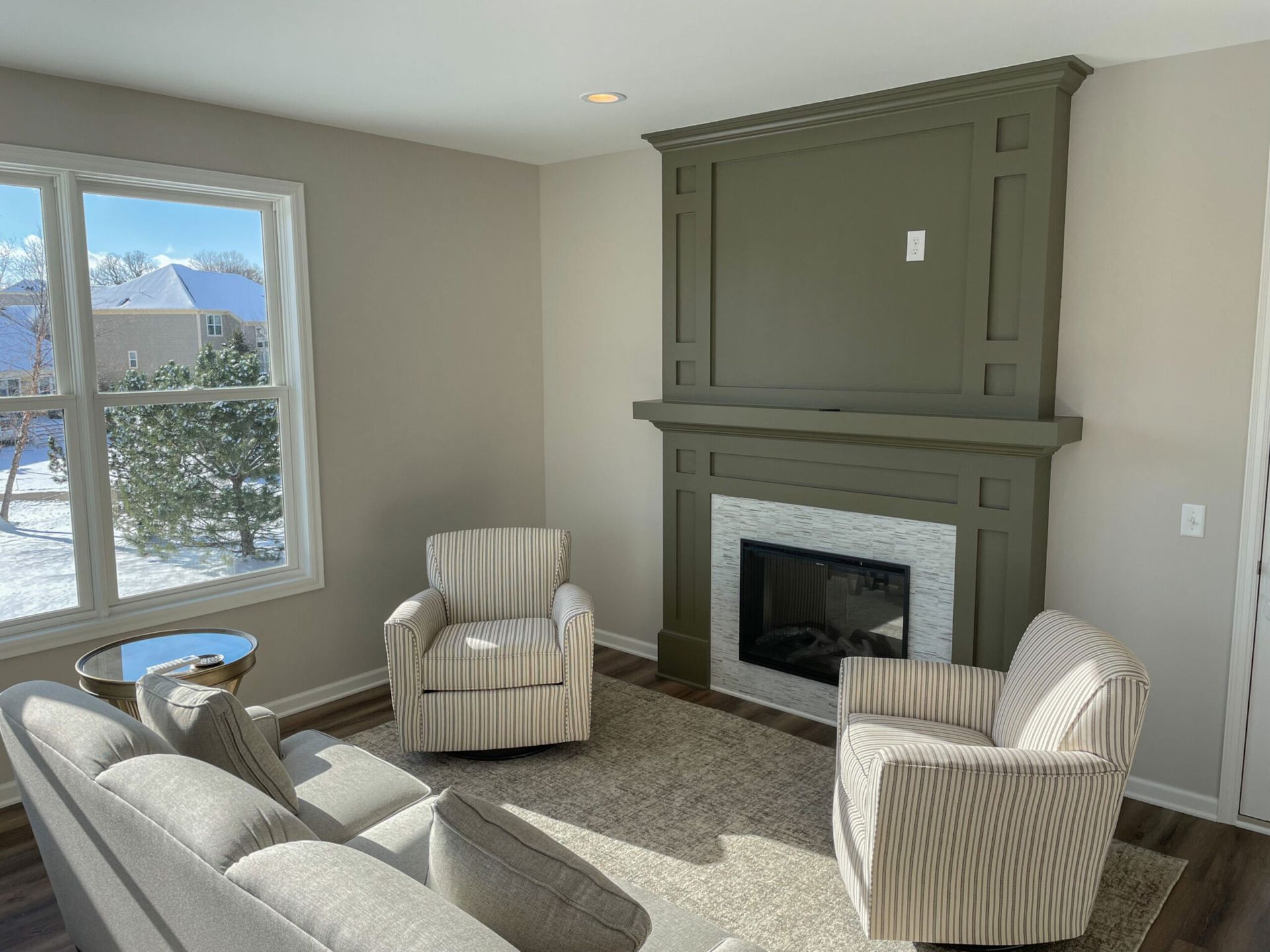 Bright living room with striped armchairs, sofa, large window, and olive-green fireplace mantel