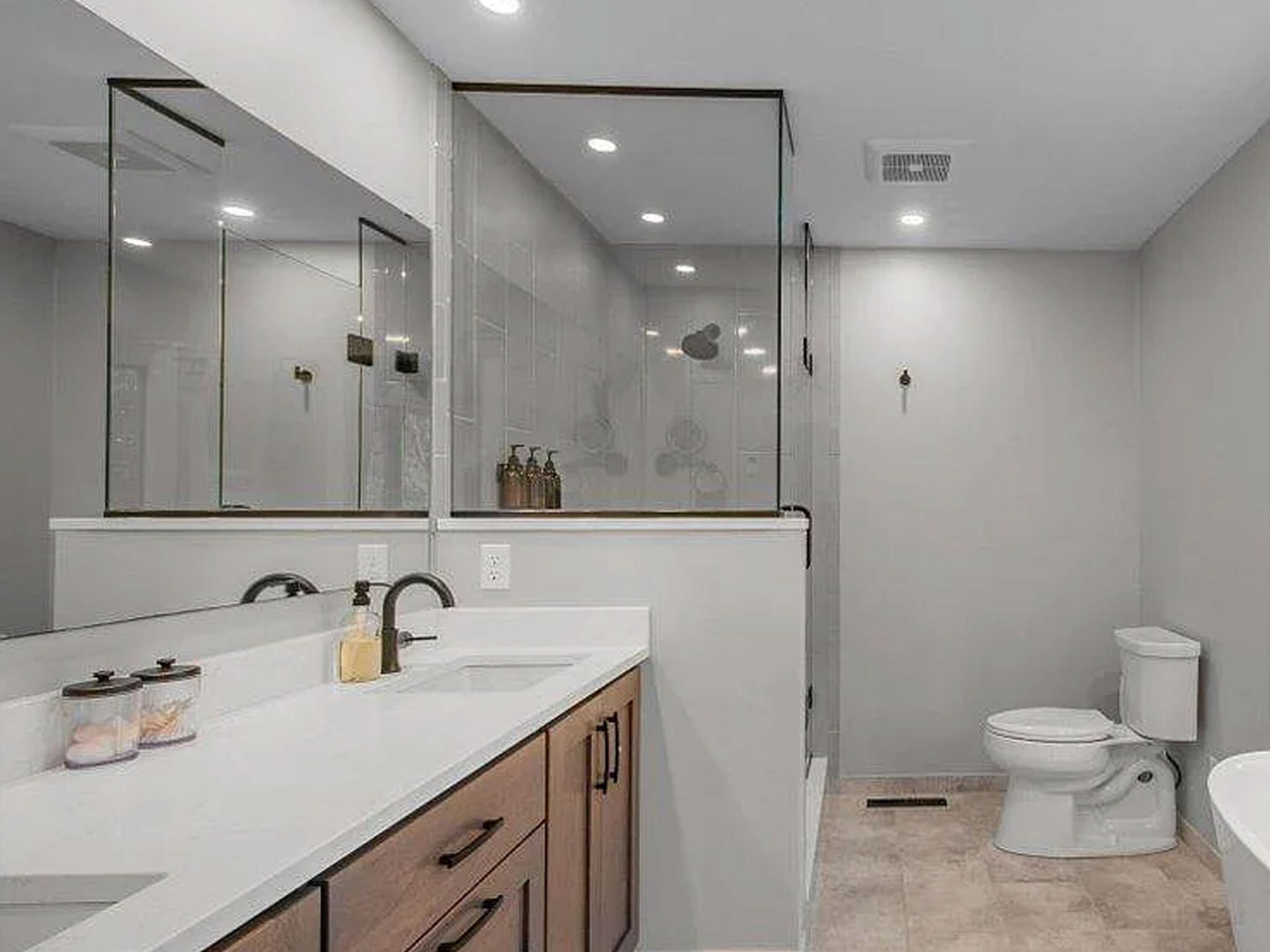 Modern bathroom with double vanity, large mirrors, glass shower, and toilet under recessed lighting Modern bathroom with double vanity, large mirrors, glass shower, and toilet under recessed lighting