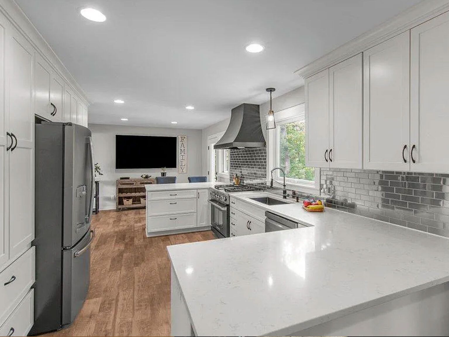 Bright modern white kitchen with stainless appliances, gray tile backsplash, and wood flooring.