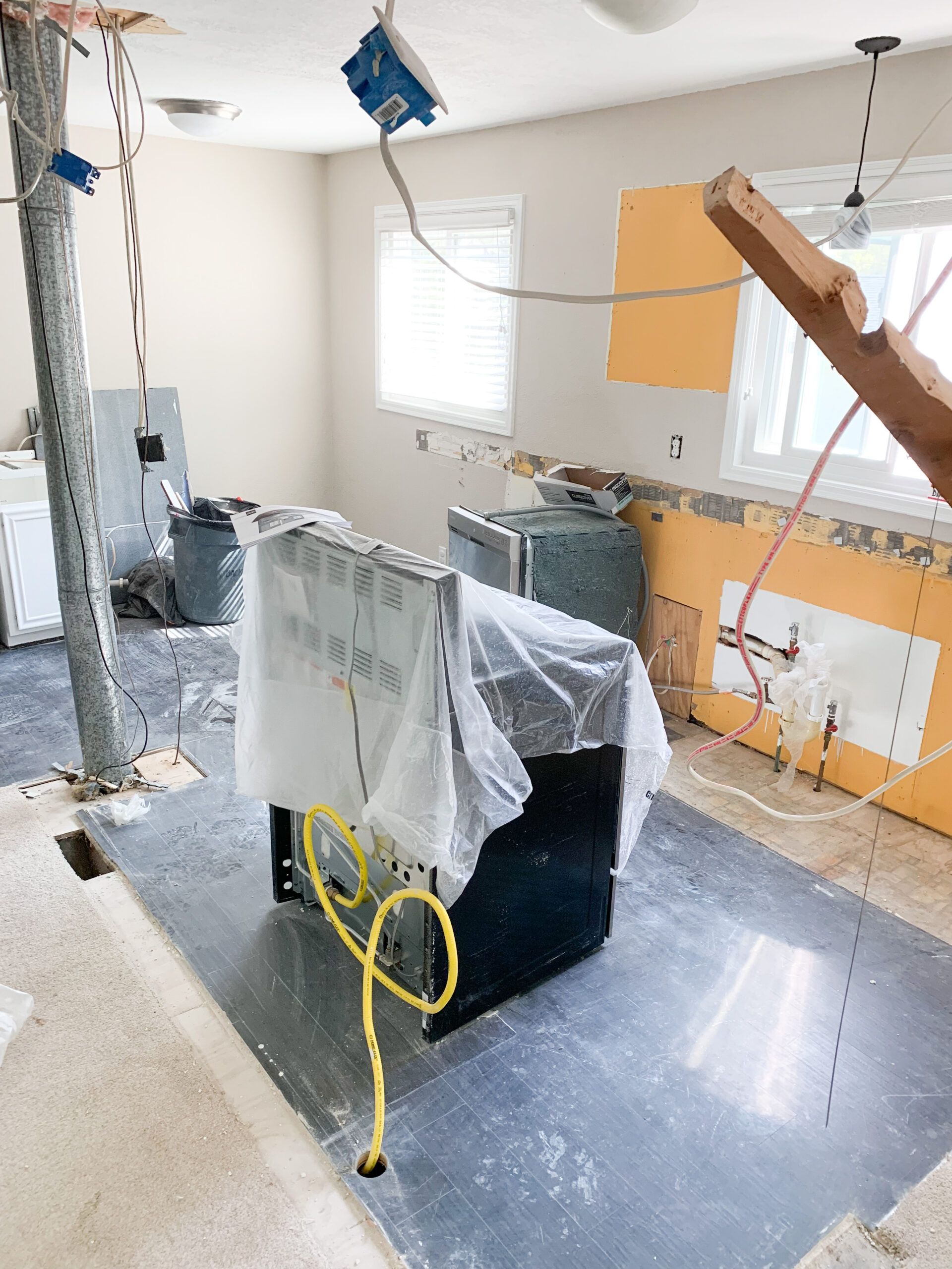 Damaged room with exposed ceiling, debris, and covered appliances during renovation or repair