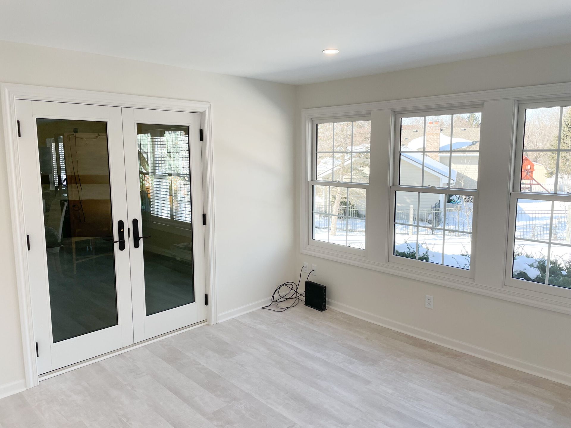 Bright empty sunroom with white walls, French doors, and large windows showing snow outside