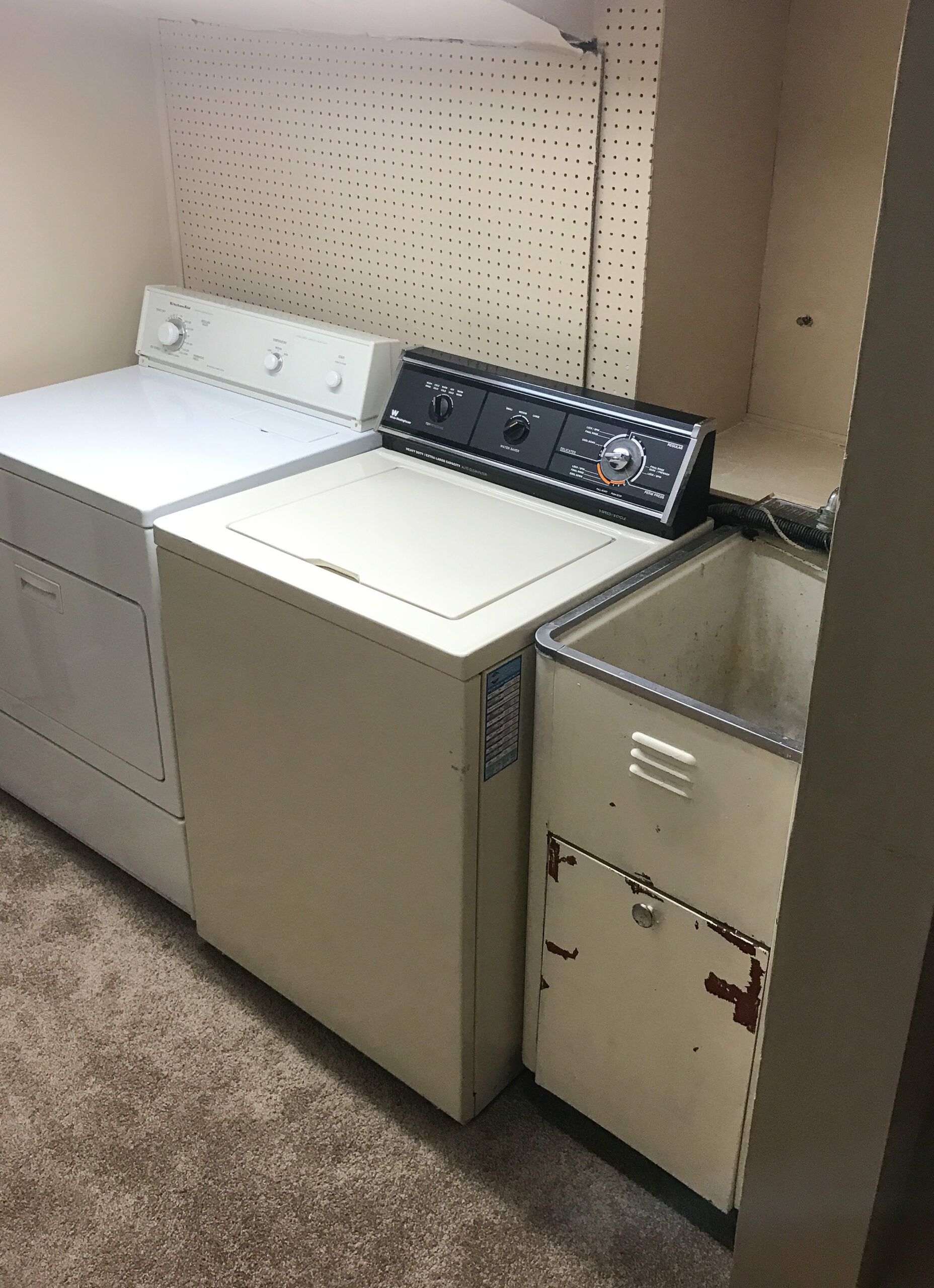 Laundry room with a washer, dryer, and utility sink against a beige wall.