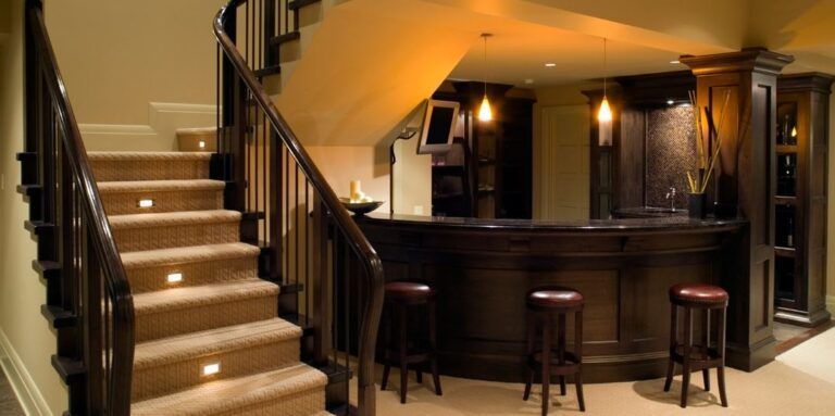 Dimly lit basement bar with curved counter, stools, and a staircase with glowing step lights