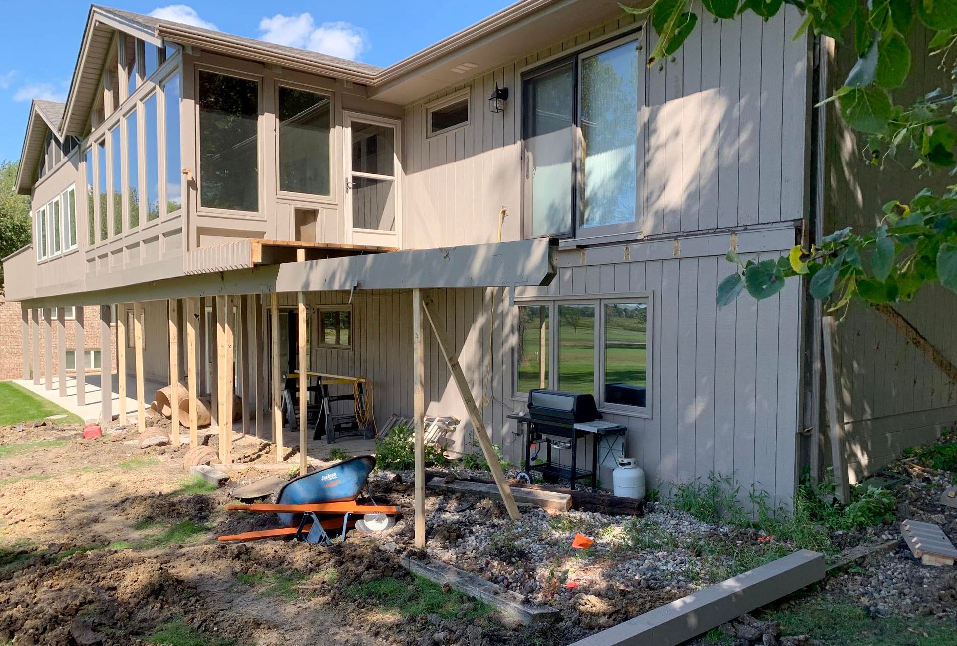 Two-story house under construction with exposed framing and support posts in a yard