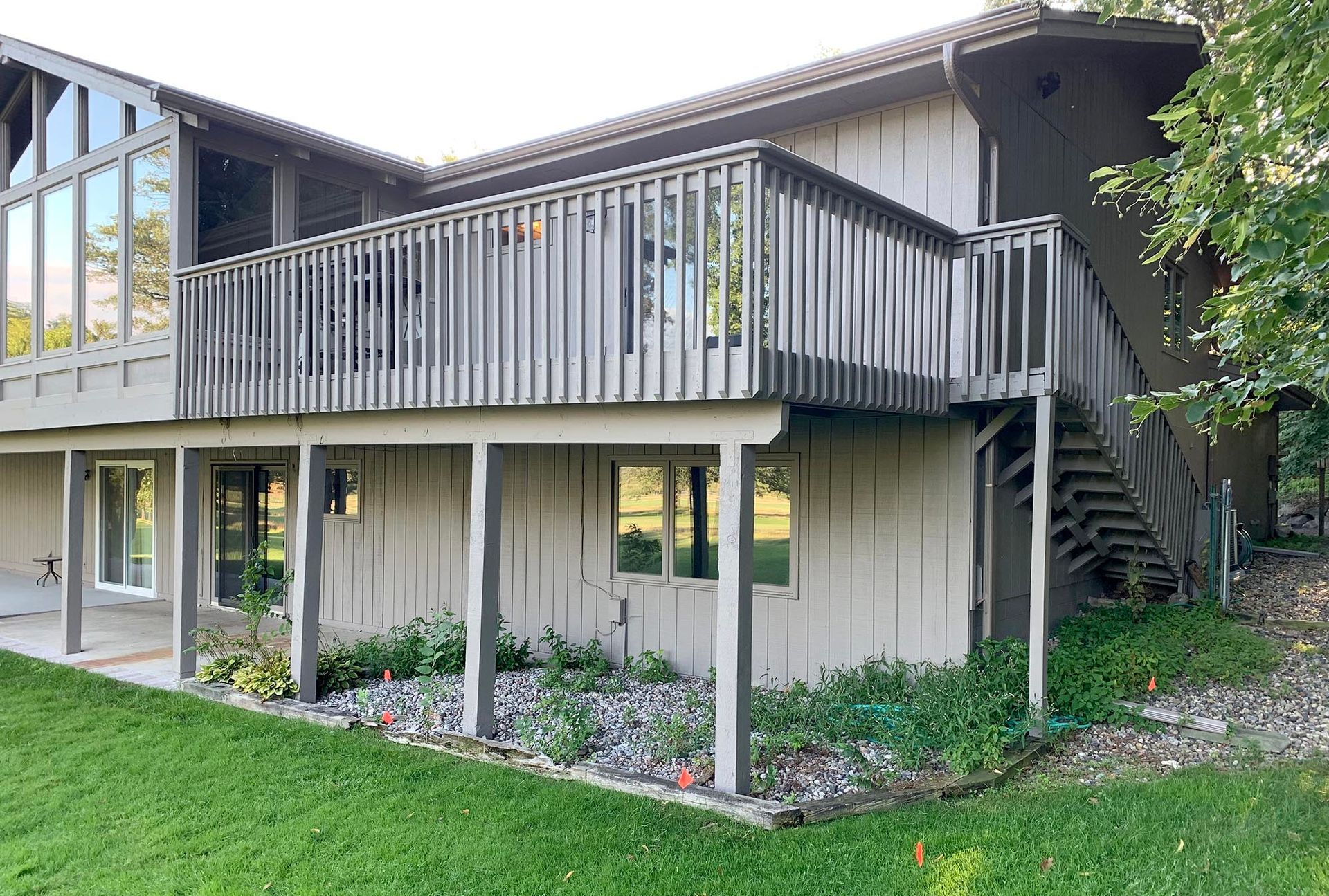 Two-story apartment building with a wooden balcony, stairs, and ground-level porch surrounded by lawn