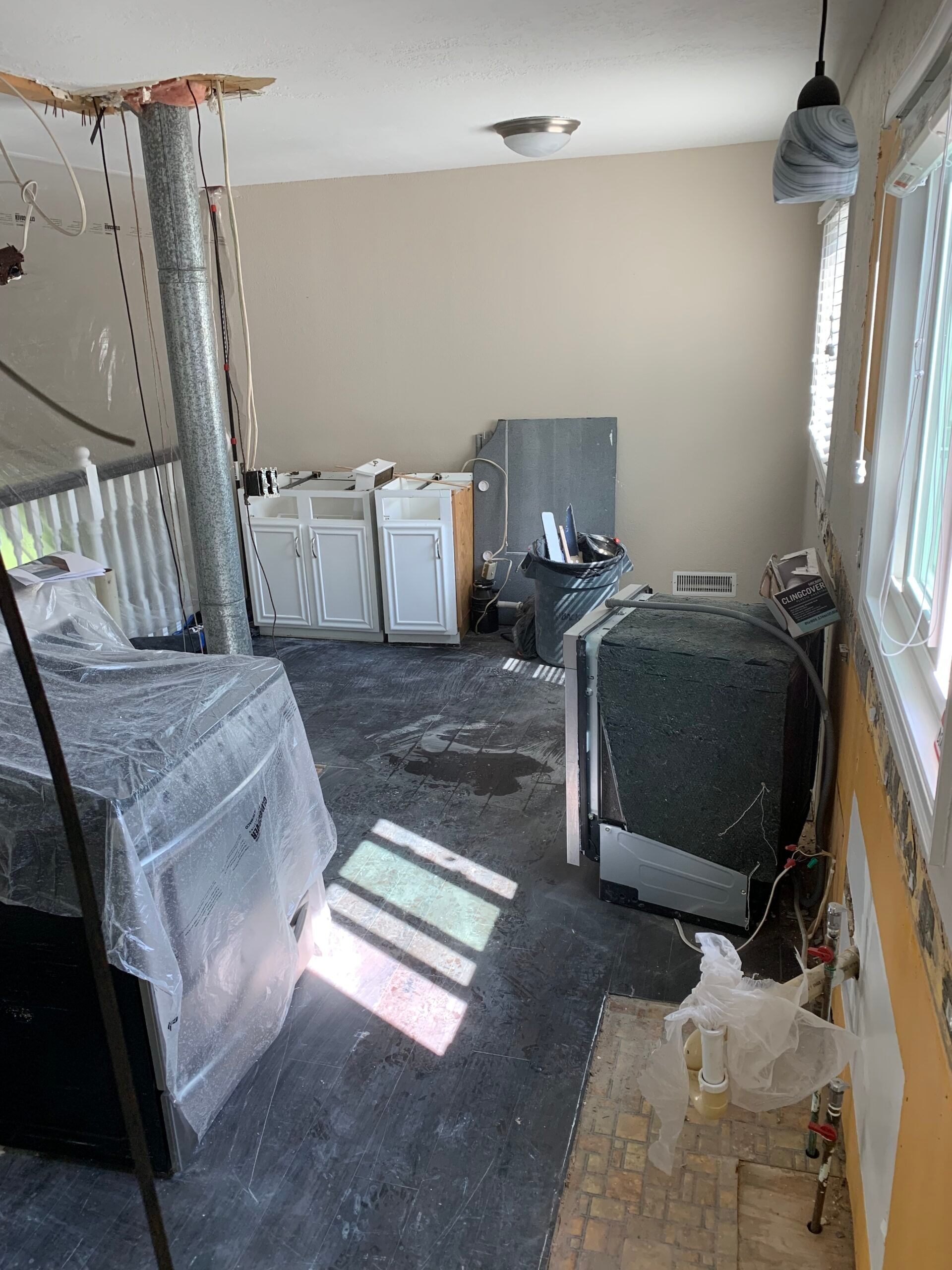 Partially renovated room with appliances, wrapped furniture, and tools on a floor covered in dust and debris