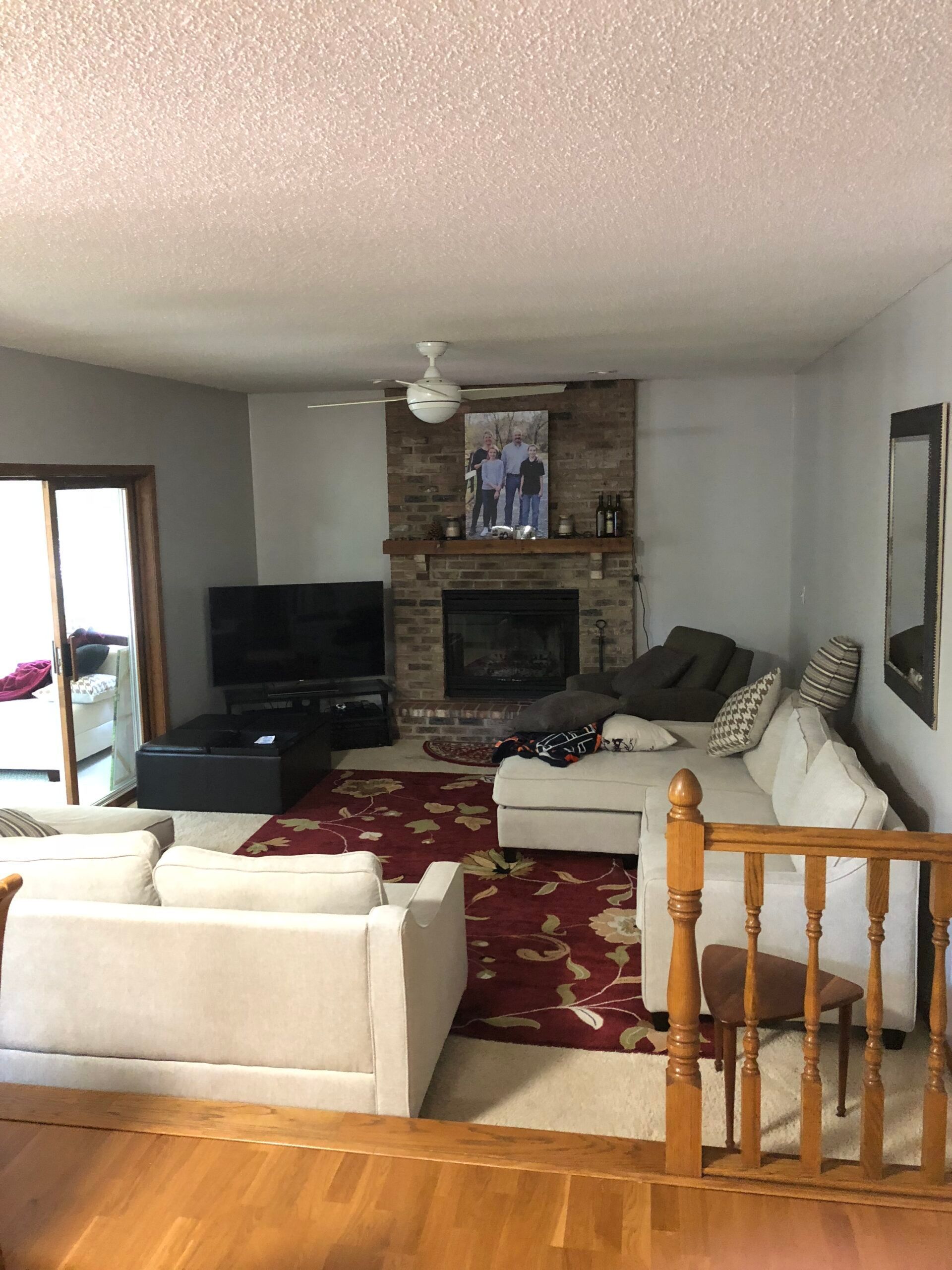 Living room with sofas, red rug, TV, and brick fireplace under a ceiling fan