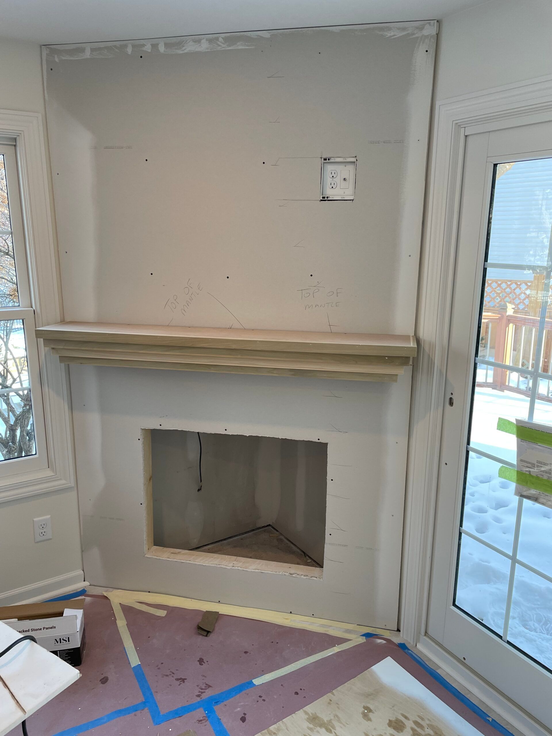 Empty room with unfinished fireplace, white walls, and large windows.