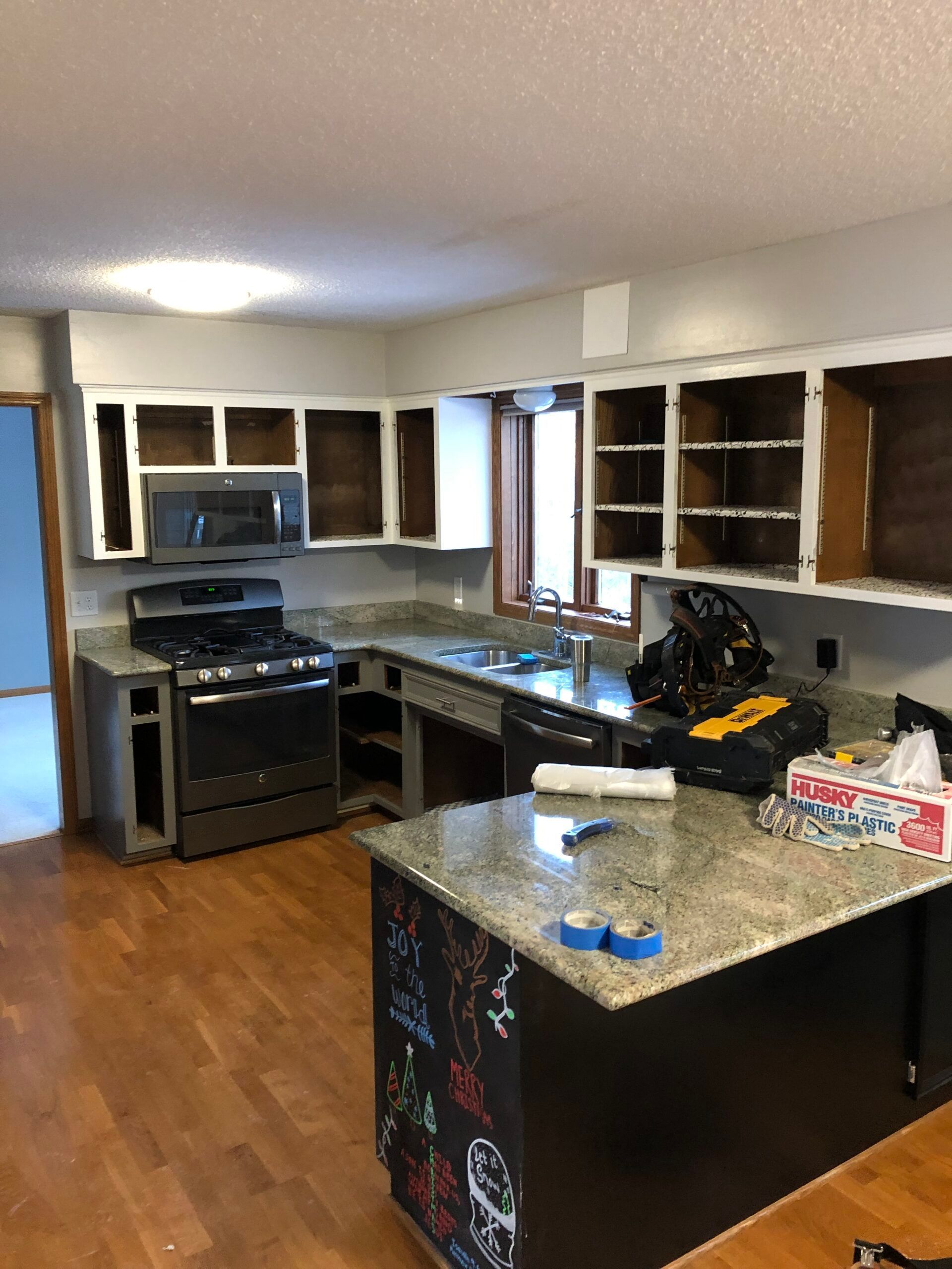 Empty kitchen with brown cabinets, granite island, and appliances on a hardwood floor.