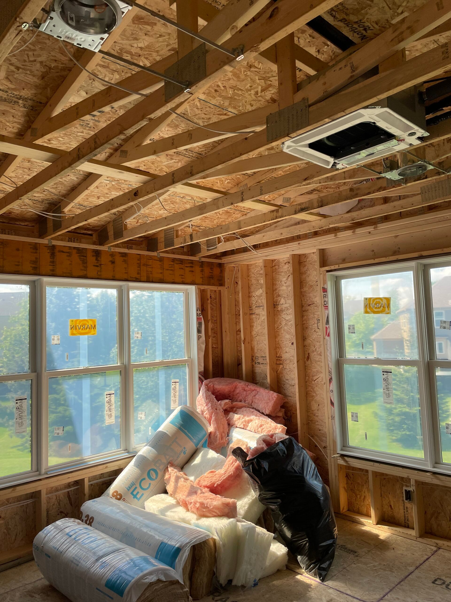 Person relaxing on a cushioned window seat in an unfinished room with exposed wooden beams and large windows.