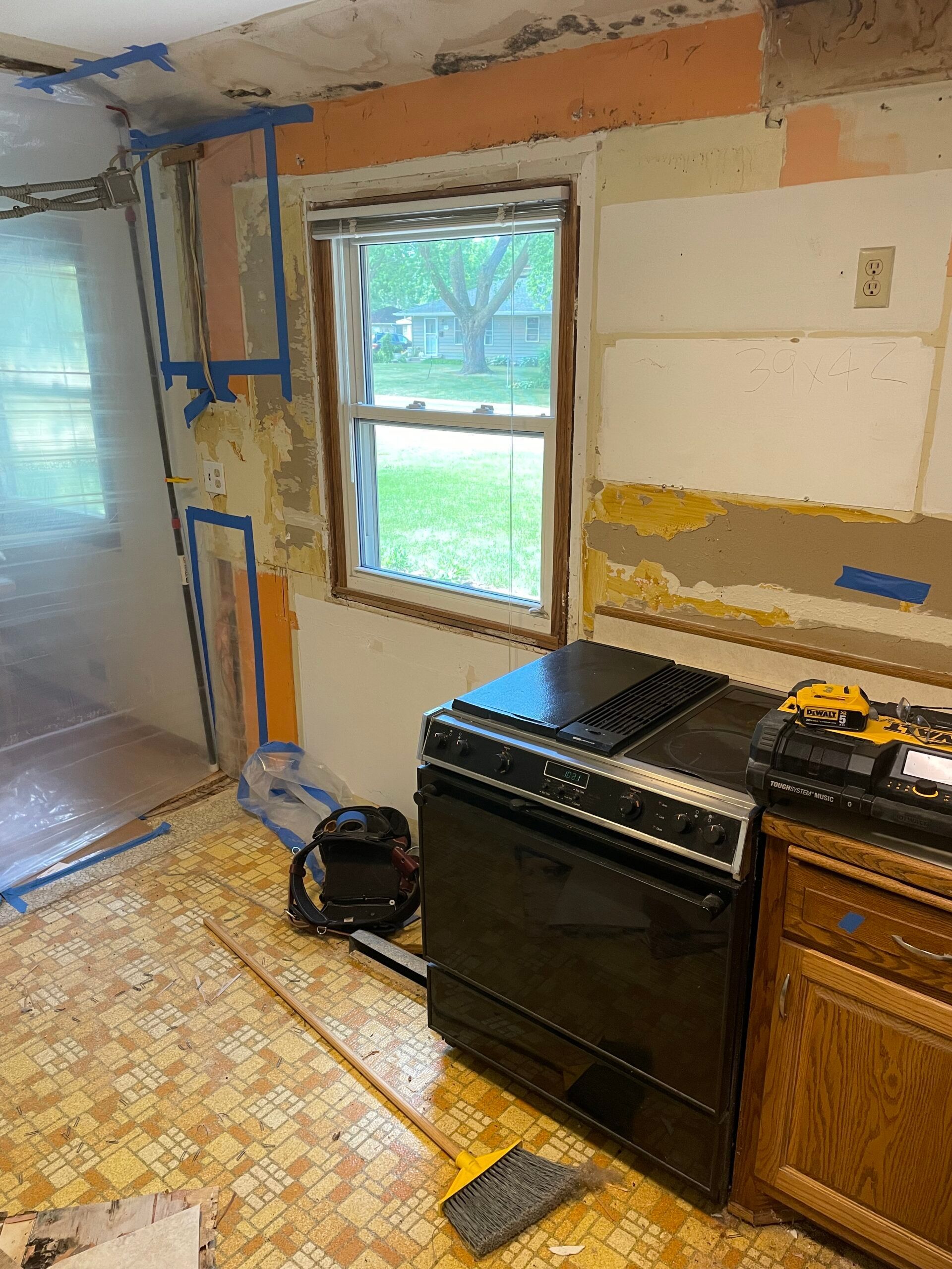 Small kitchen under renovation with exposed walls, a window, stove, and tools on the floor