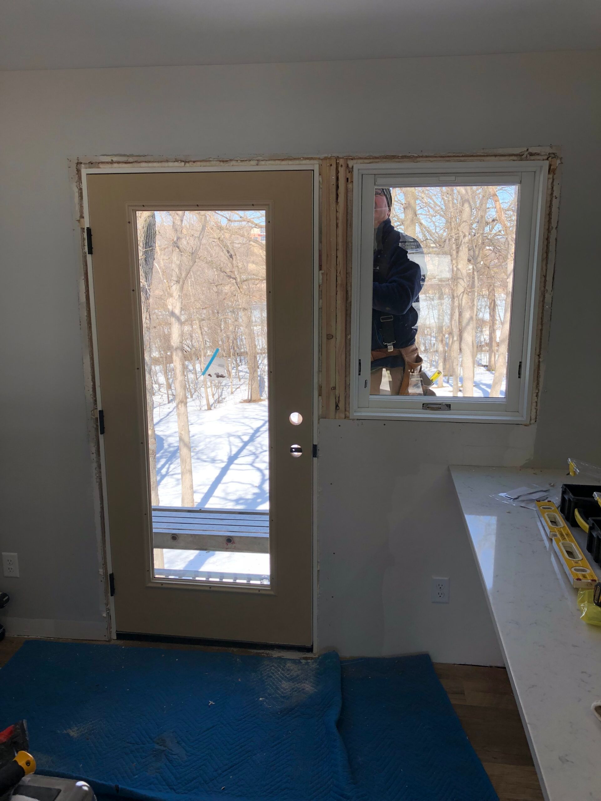 Unfinished room with a door and window, blue floor covering, and snow visible outside.