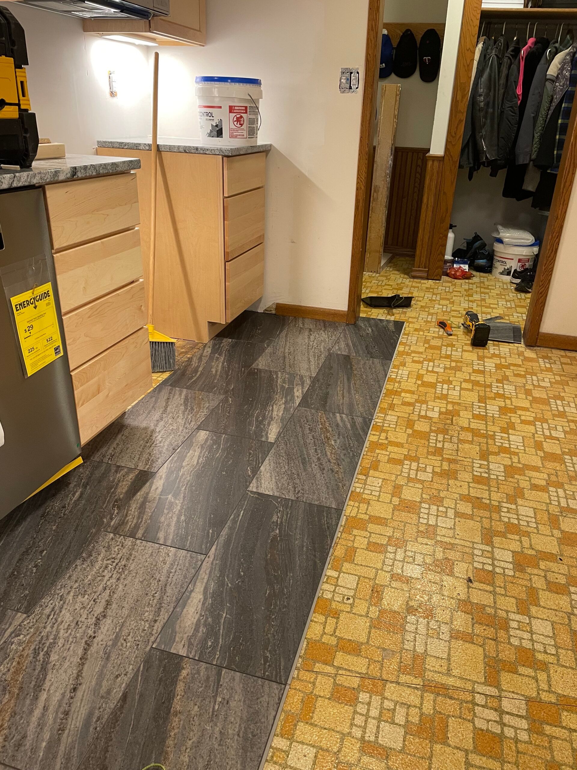 Kitchen with wood cabinets, dark flooring, and a doorway to a cluttered hall with a coat closet.