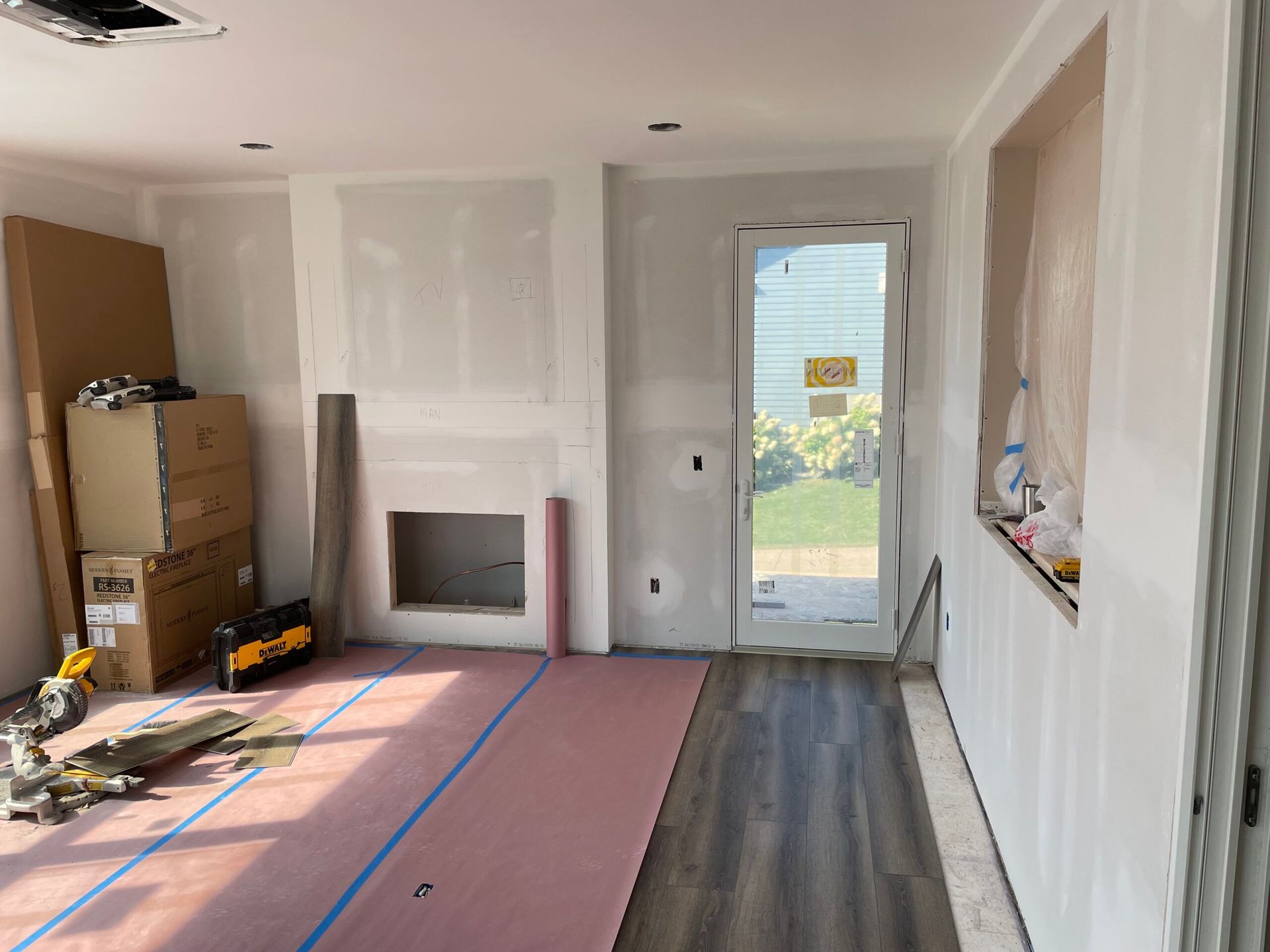 Unfinished room interior with drywall, a fireplace, and a glass door opening to a bright yard.