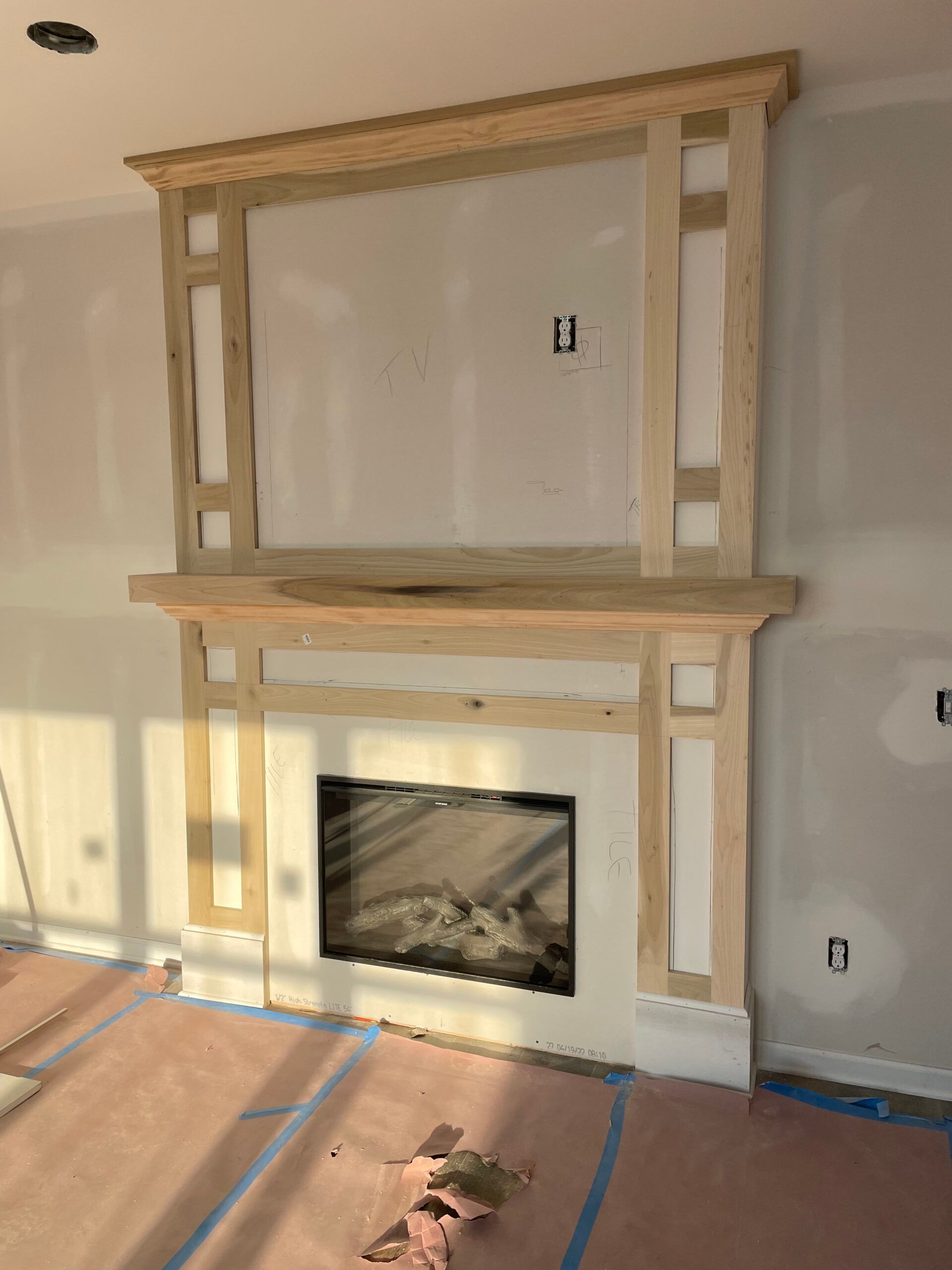 Partially built fireplace wall with unfinished wood trim in a sunlit room