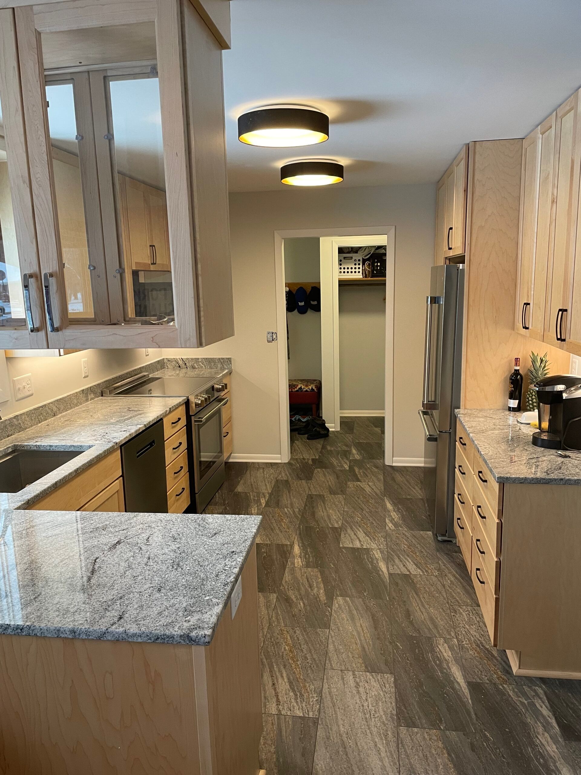 Narrow kitchen with gray cabinets, granite counters, wood floors, and two ceiling lights.