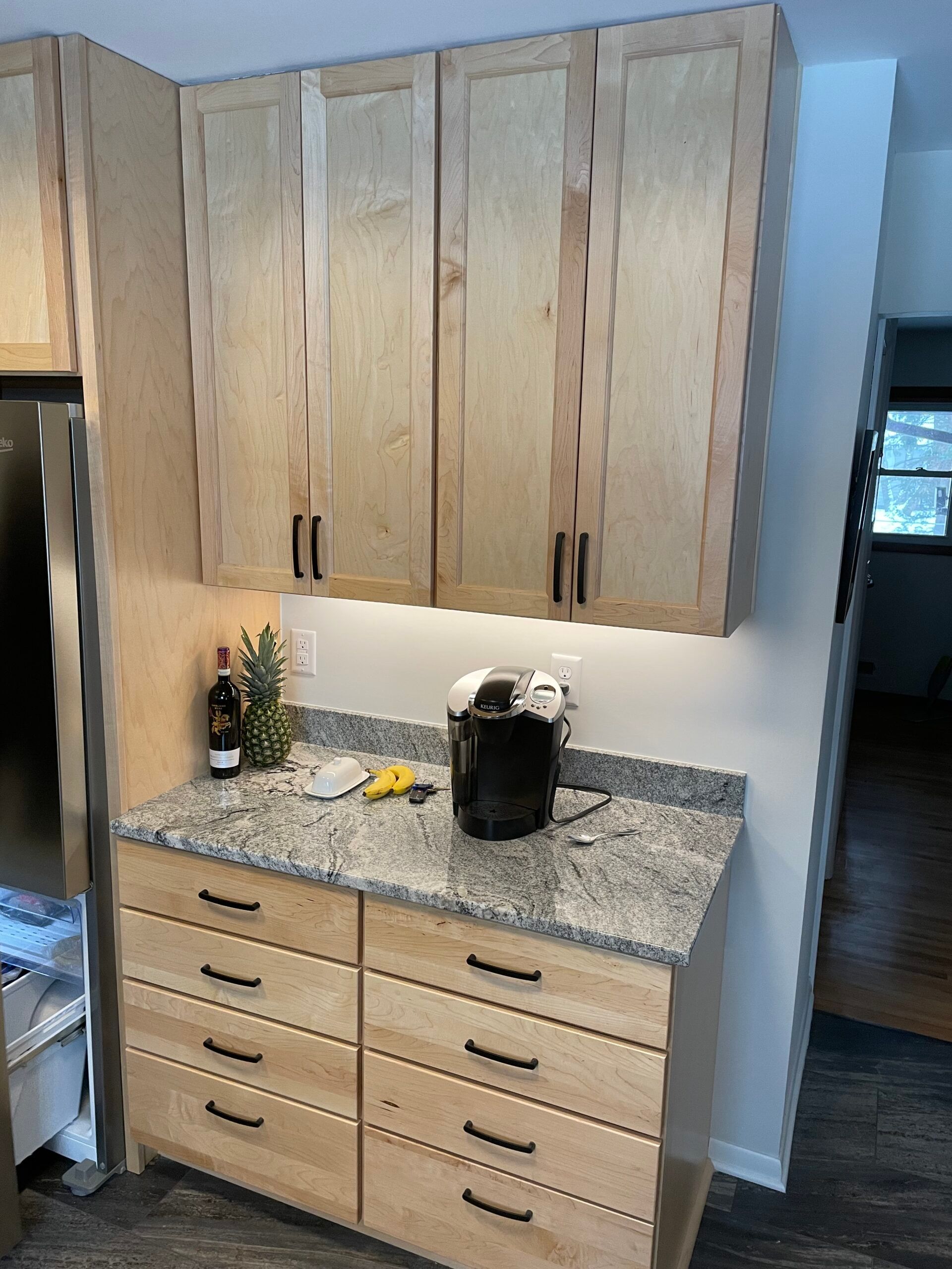 Kitchen cabinets and drawers in light wood with a granite countertop, coffee maker, and small decor items