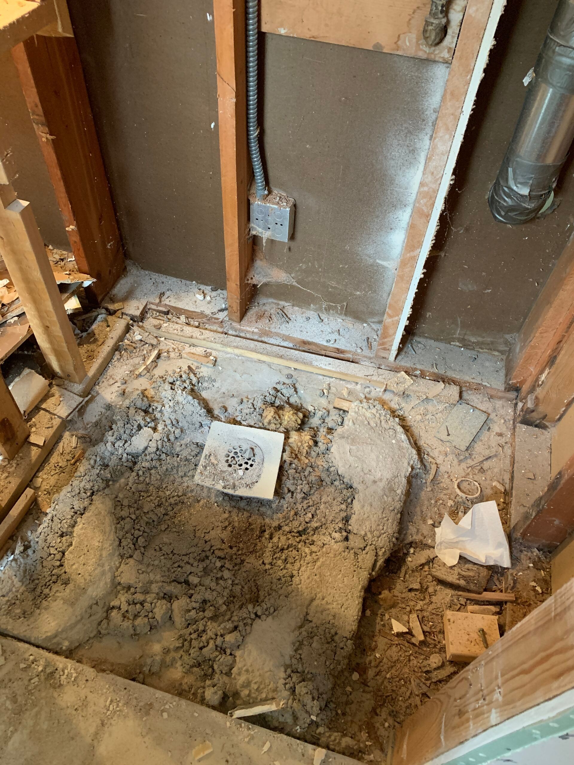 Renovation site with exposed floor joists, broken concrete, and a drain pipe opening in a bathroom floor