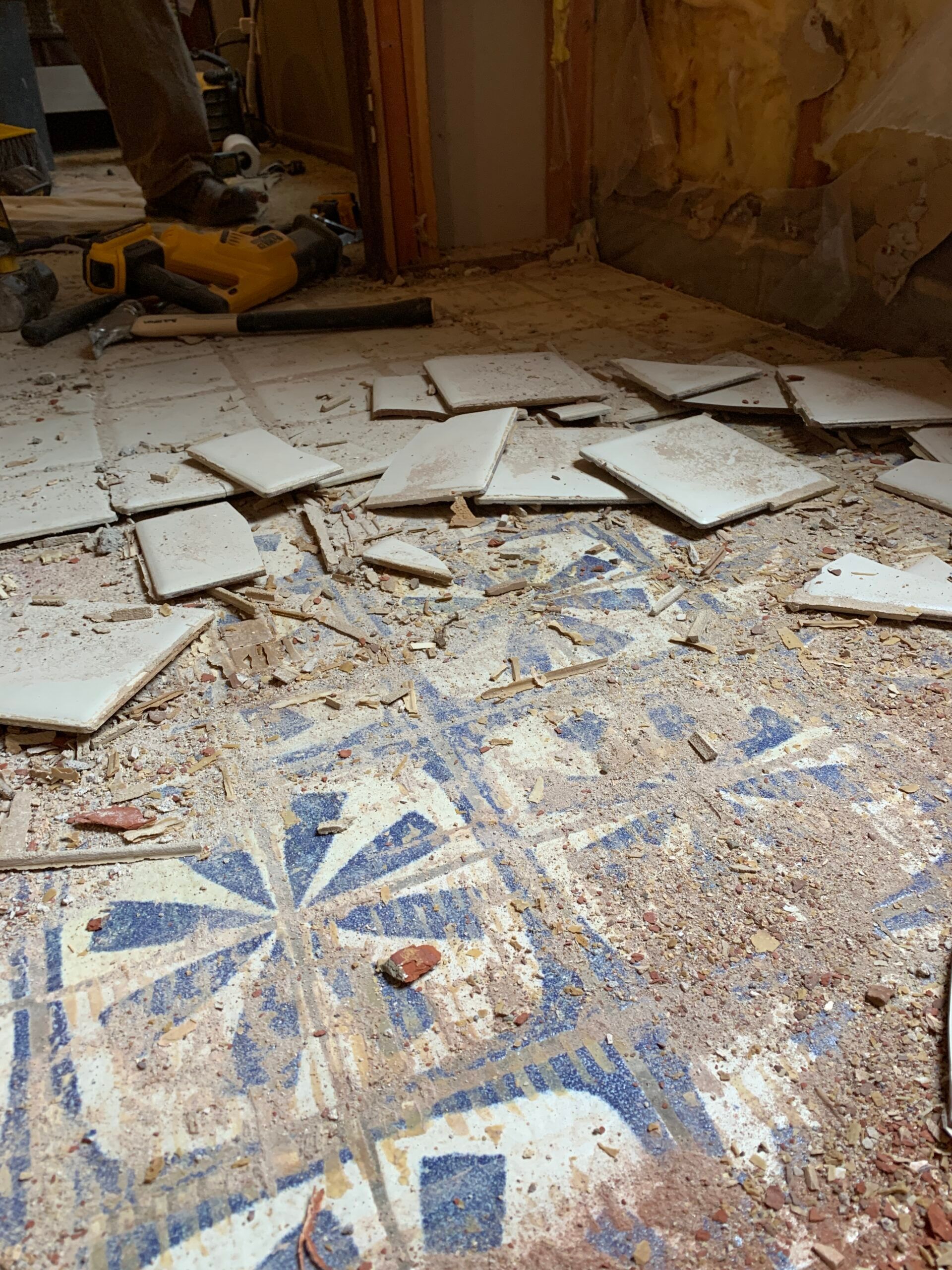 Damaged tiled floor with broken white tiles and blue mosaic pattern in a debris-filled room