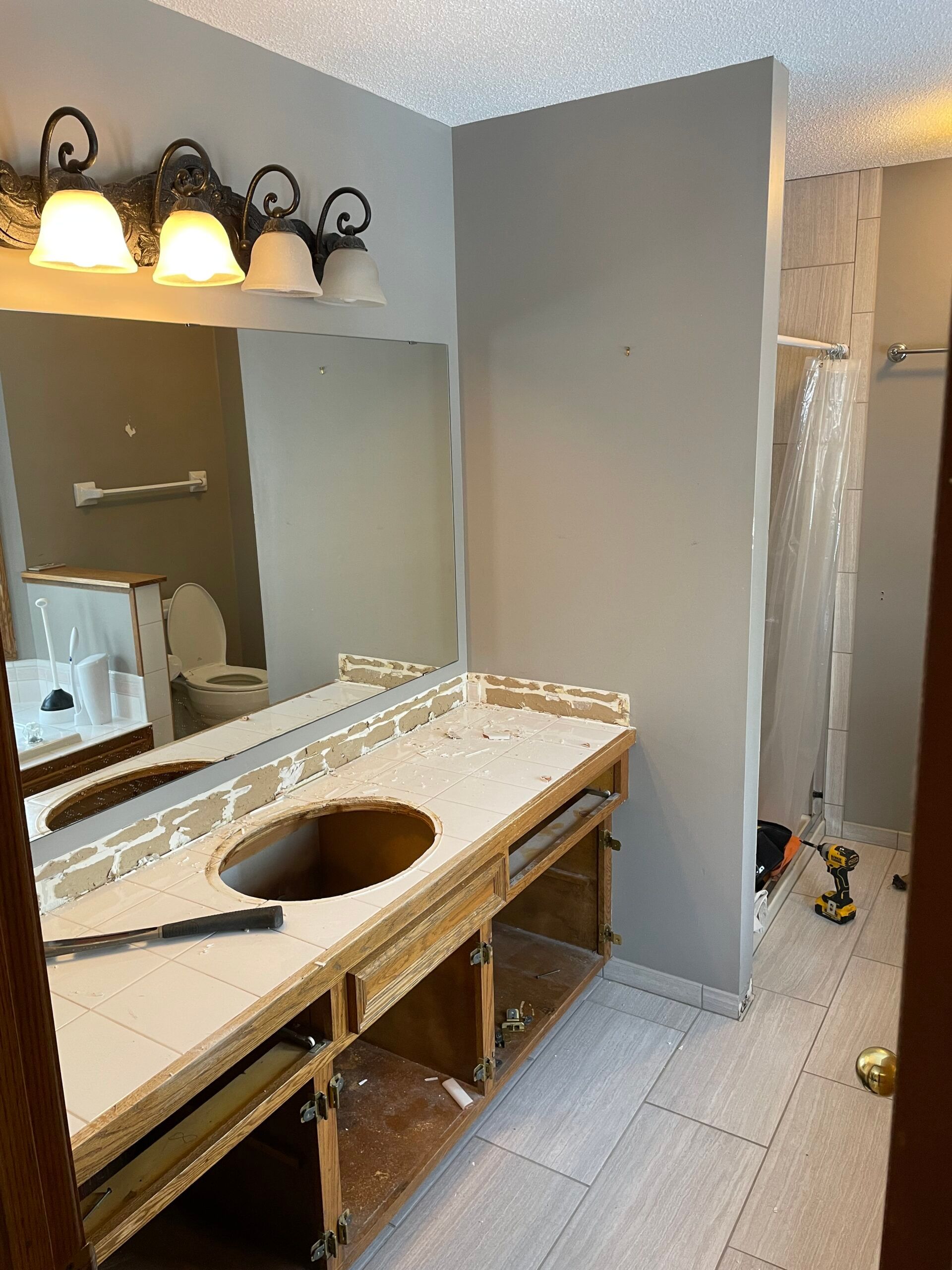 Bathroom vanity under renovation with sink removed, mirror, and lights above a countertop.