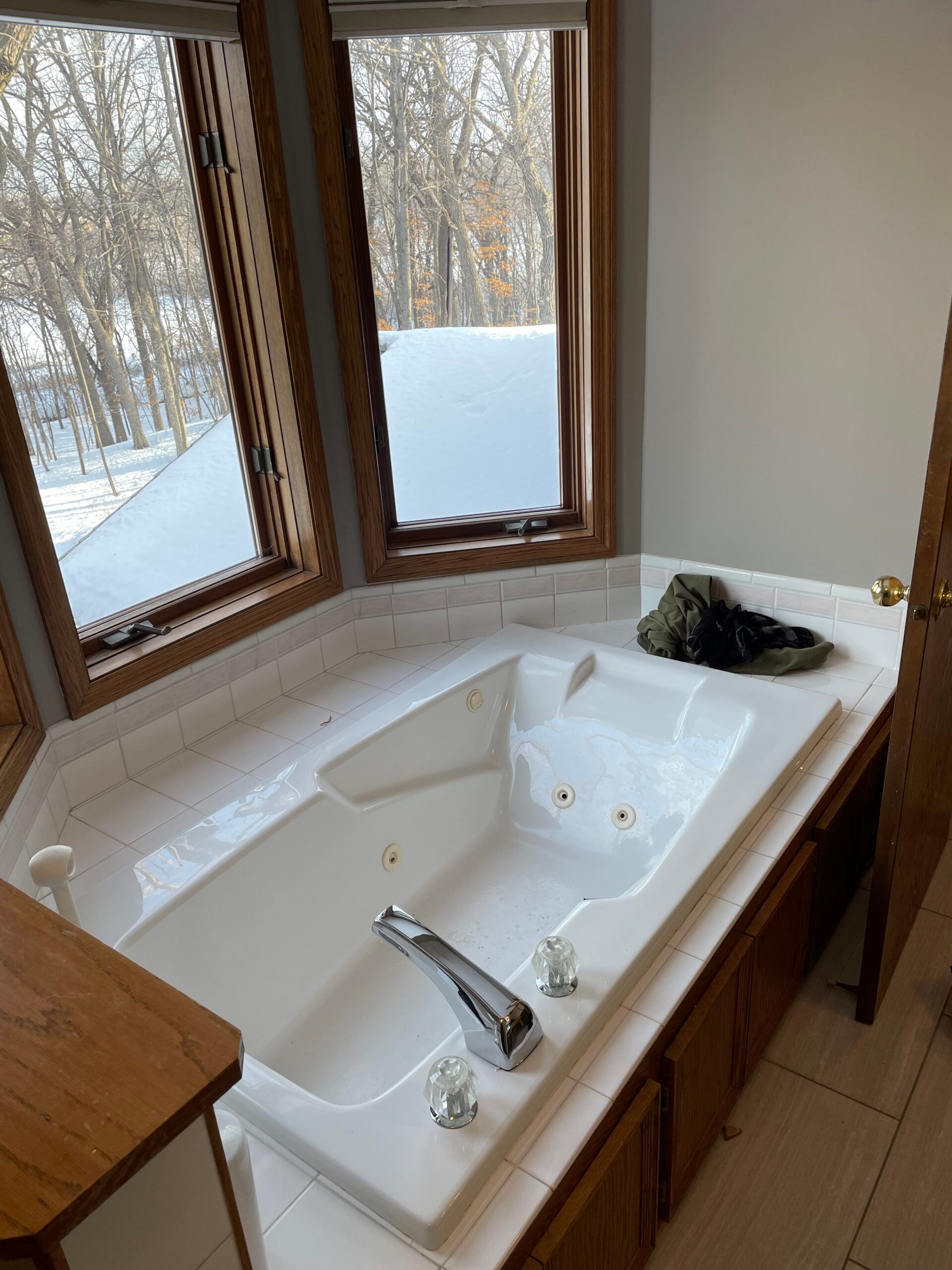 Corner bathtub by a window overlooking snowy trees, with a towel and toiletries nearby