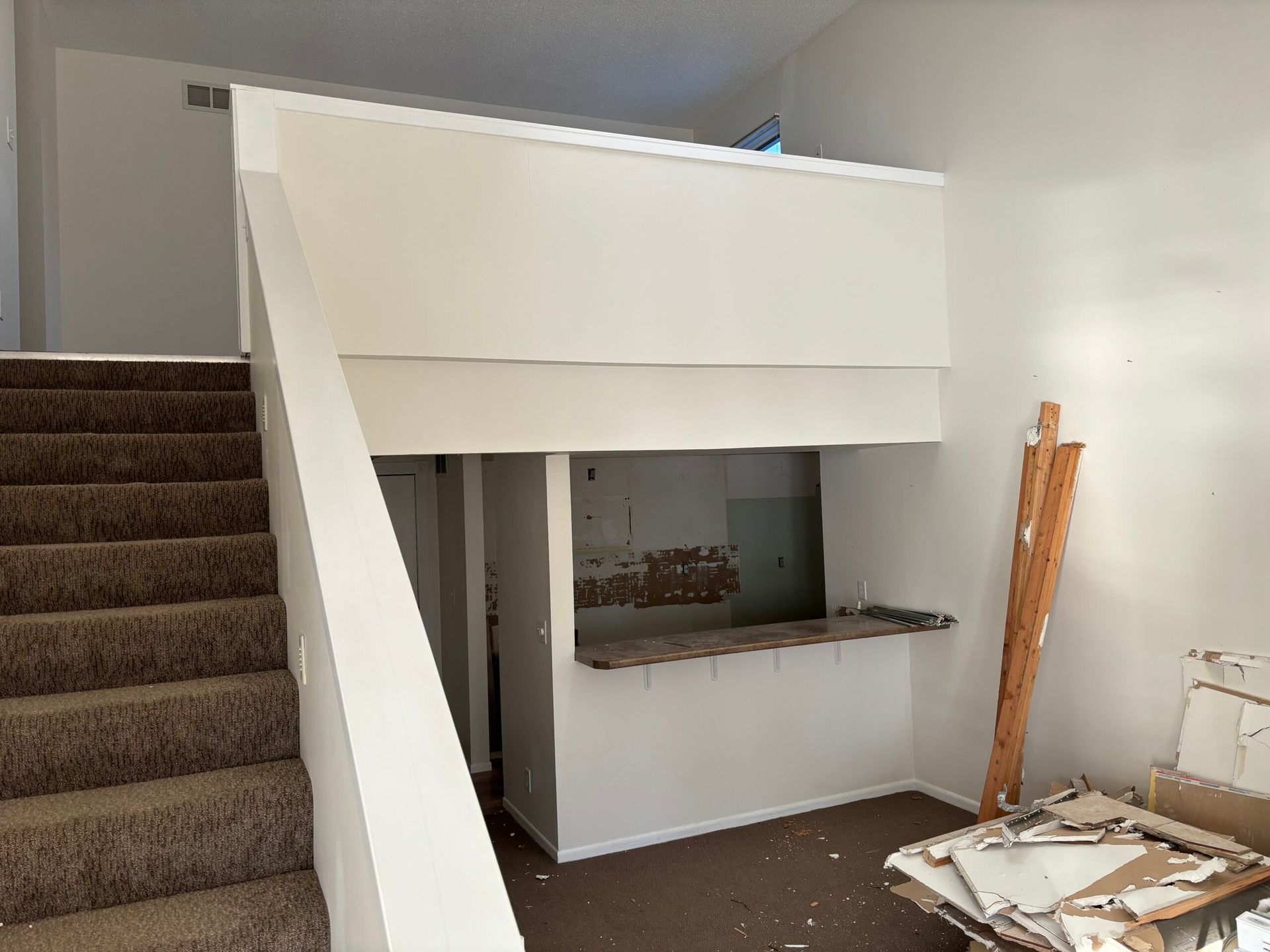 Staircase beside a white half-wall and pass-through in a partially renovated room with construction debris.