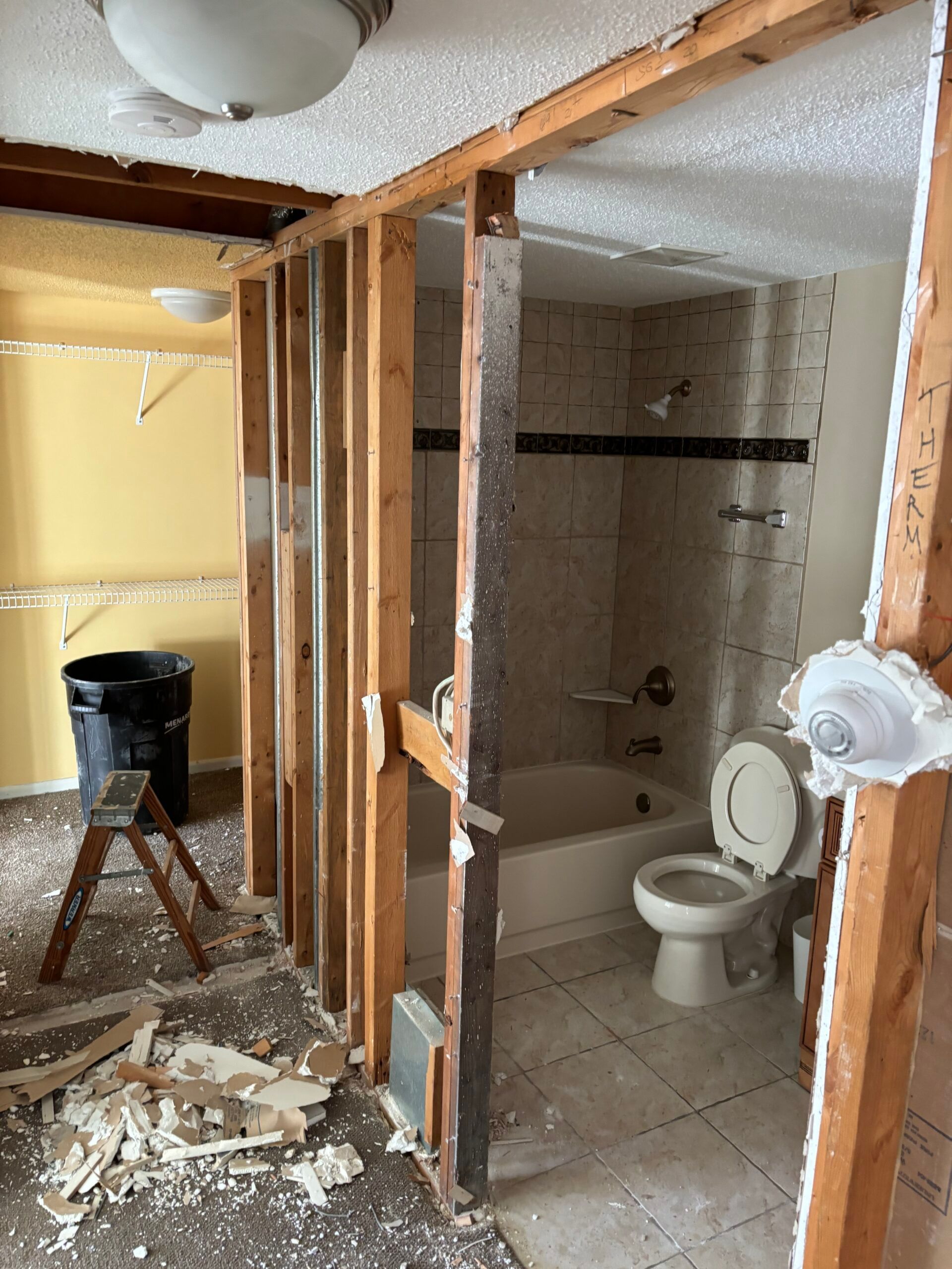 Partially demolished bathroom with exposed studs, toilet, tub, and debris on the floor