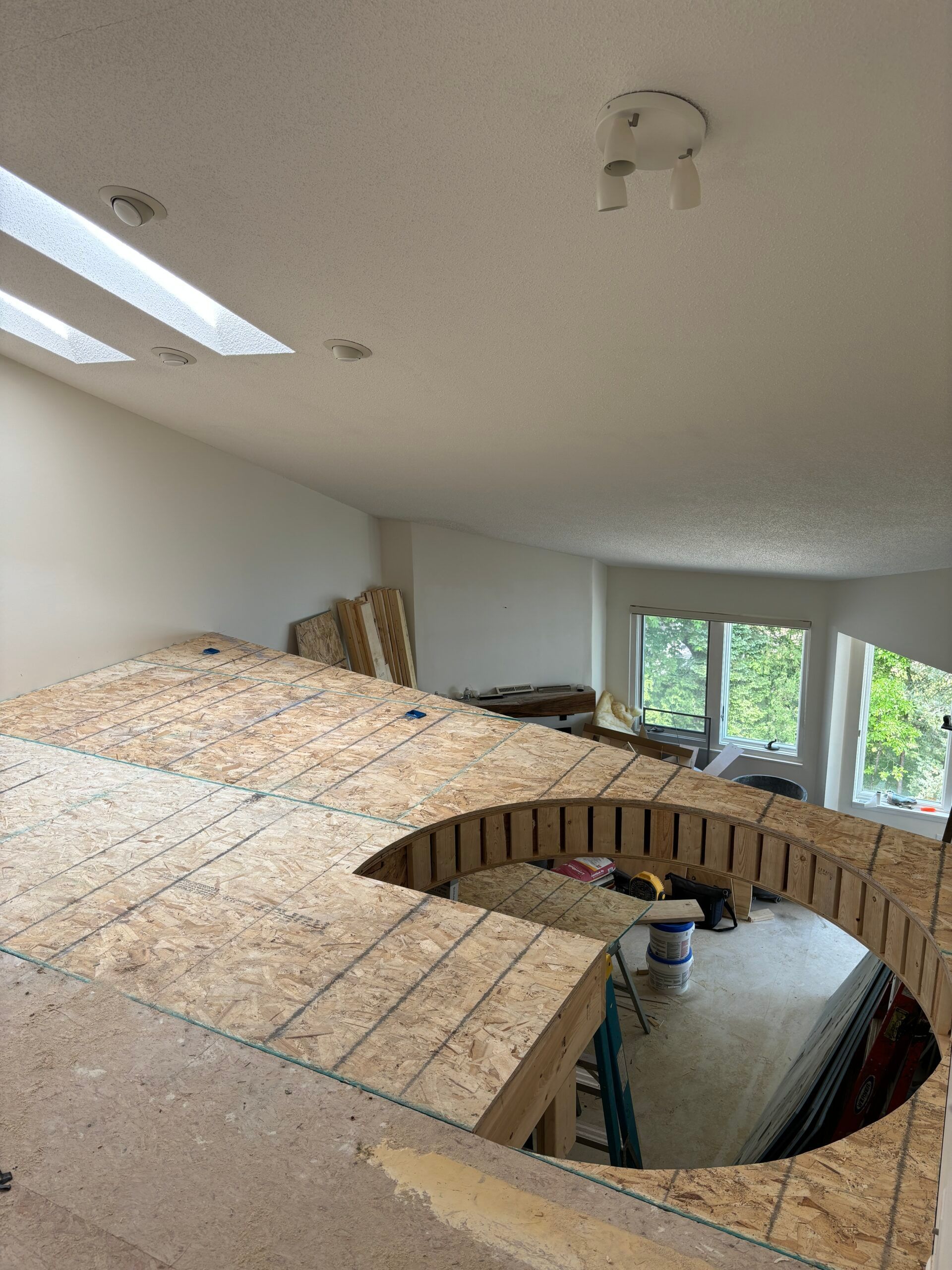 Indoor room with large circular floor opening and exposed wood framing under construction