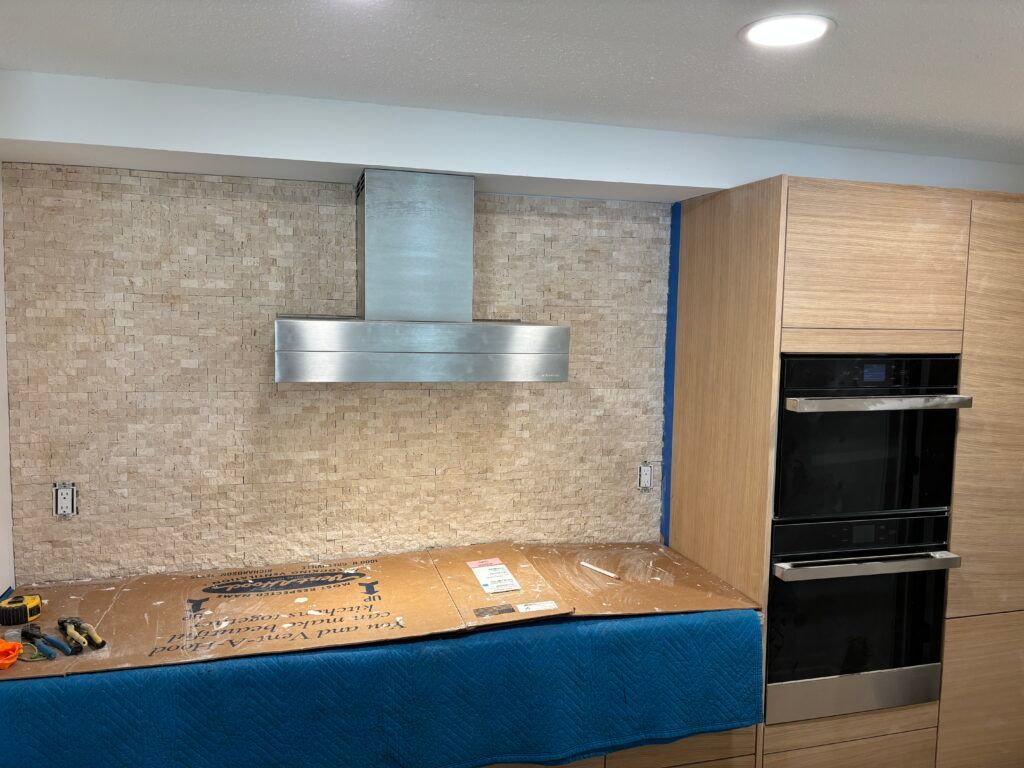 Kitchen under renovation with blue-covered cabinets, stone backsplash, and built-in oven.
